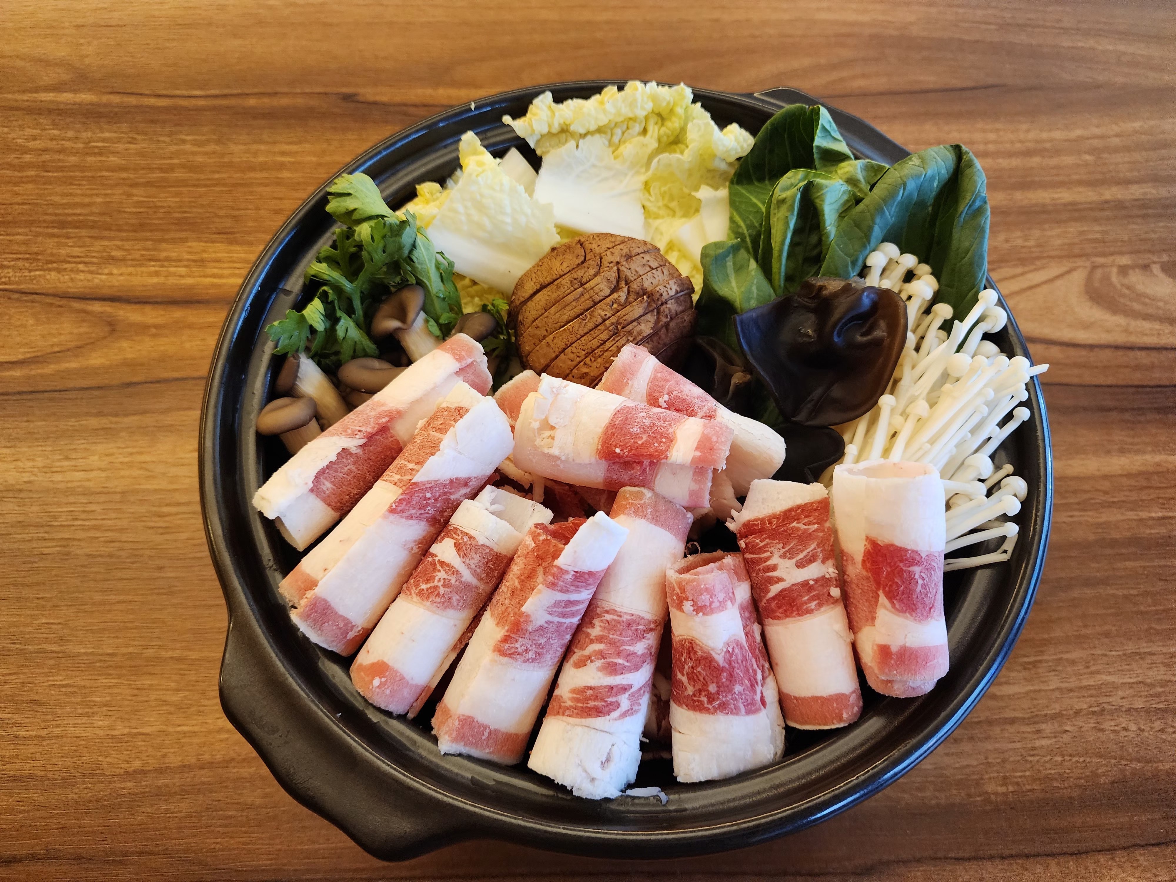 Raw thinly sliced pork belly arranged with napa cabbage, shiitake mushrooms, and enoki mushrooms in a pot