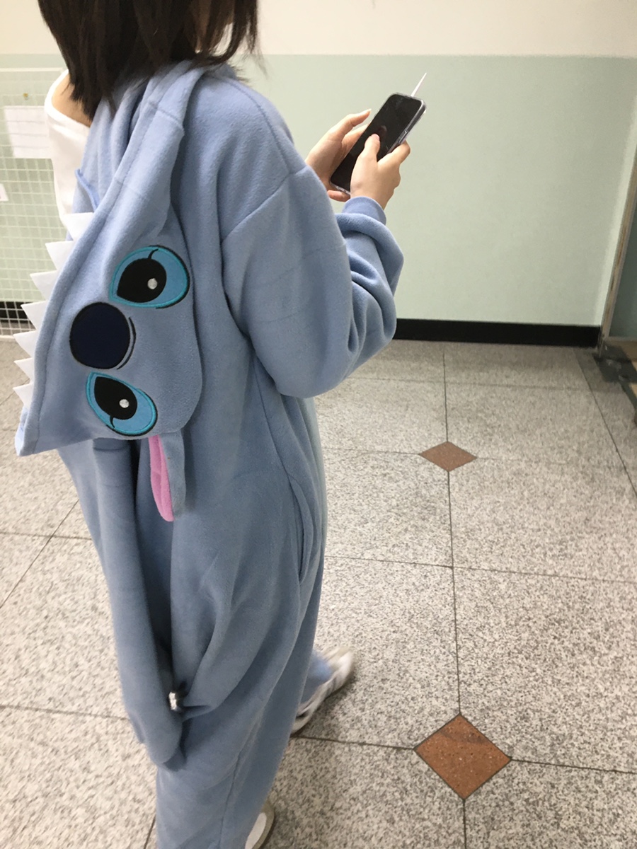 A person wearing a light blue character onesie standing in an indoor studio hallway.