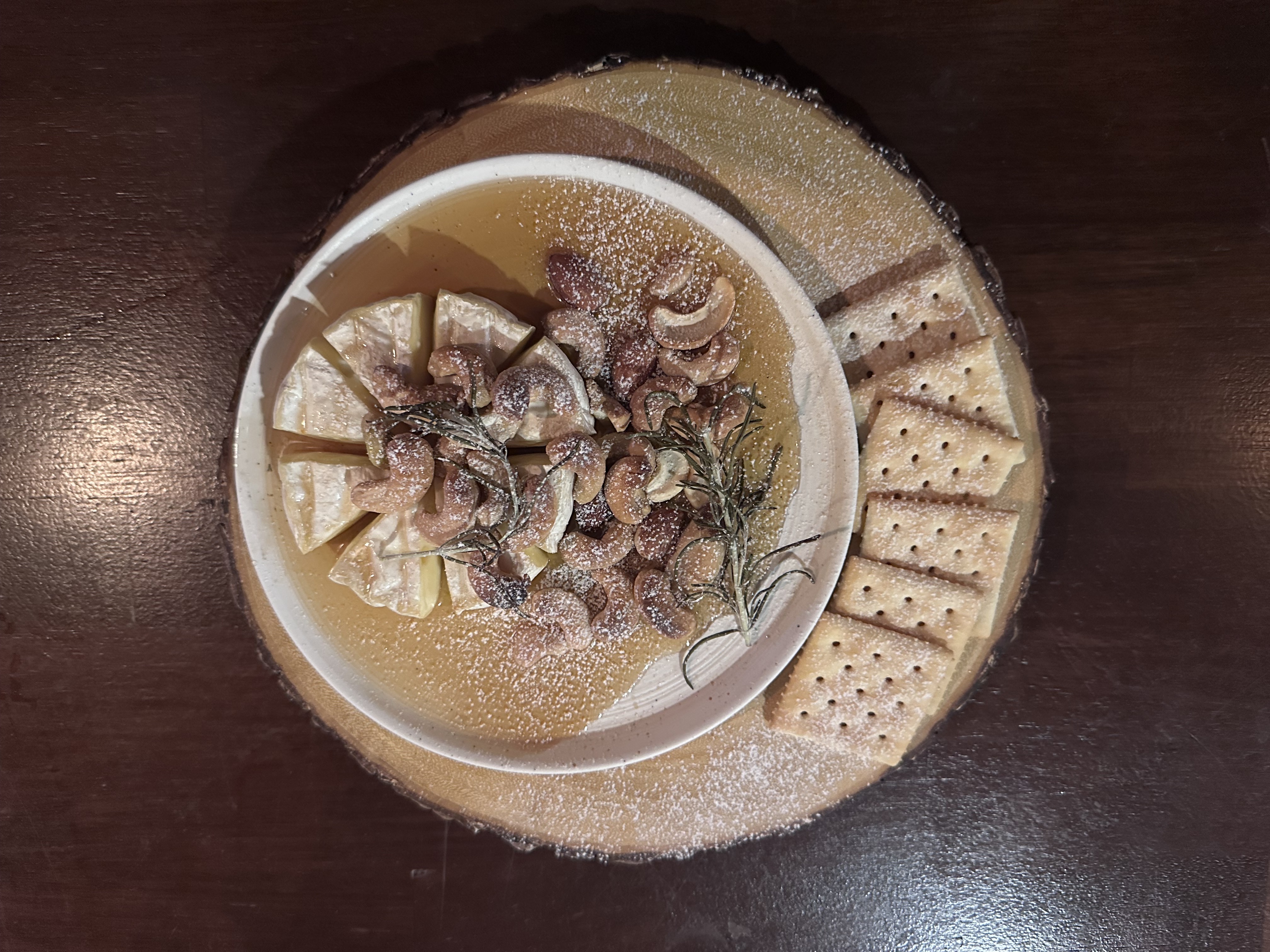 Brie cheese with nuts, honey, and rosemary served on a wooden board