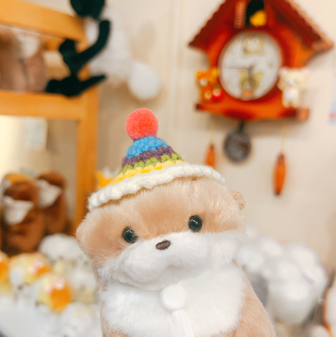 Plush animal character wearing a handmade knit pom-pom hat on wooden shelf