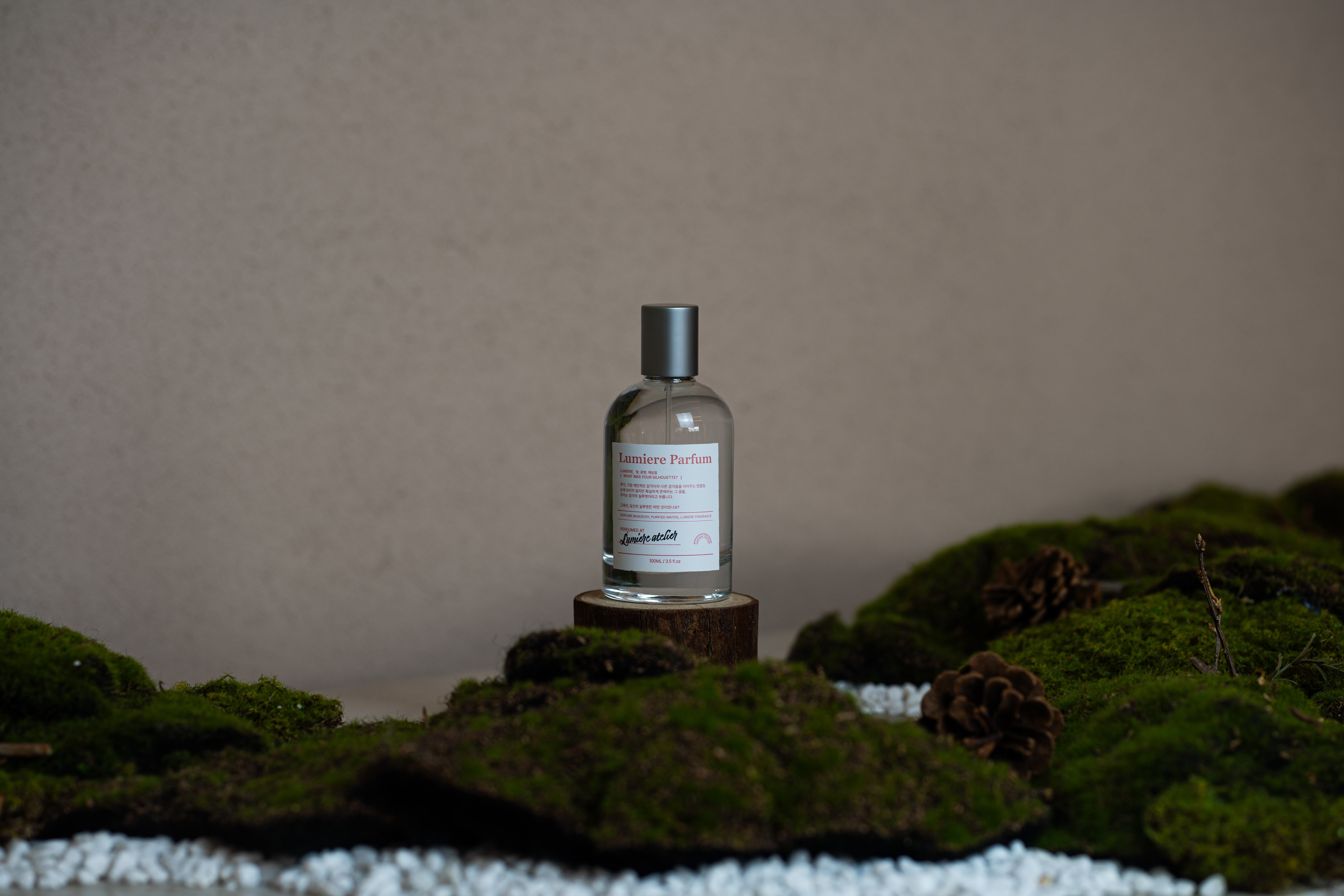 Lumiere Parfum bottle standing on a wooden pedestal surrounded by botanical moss and white pebbles
