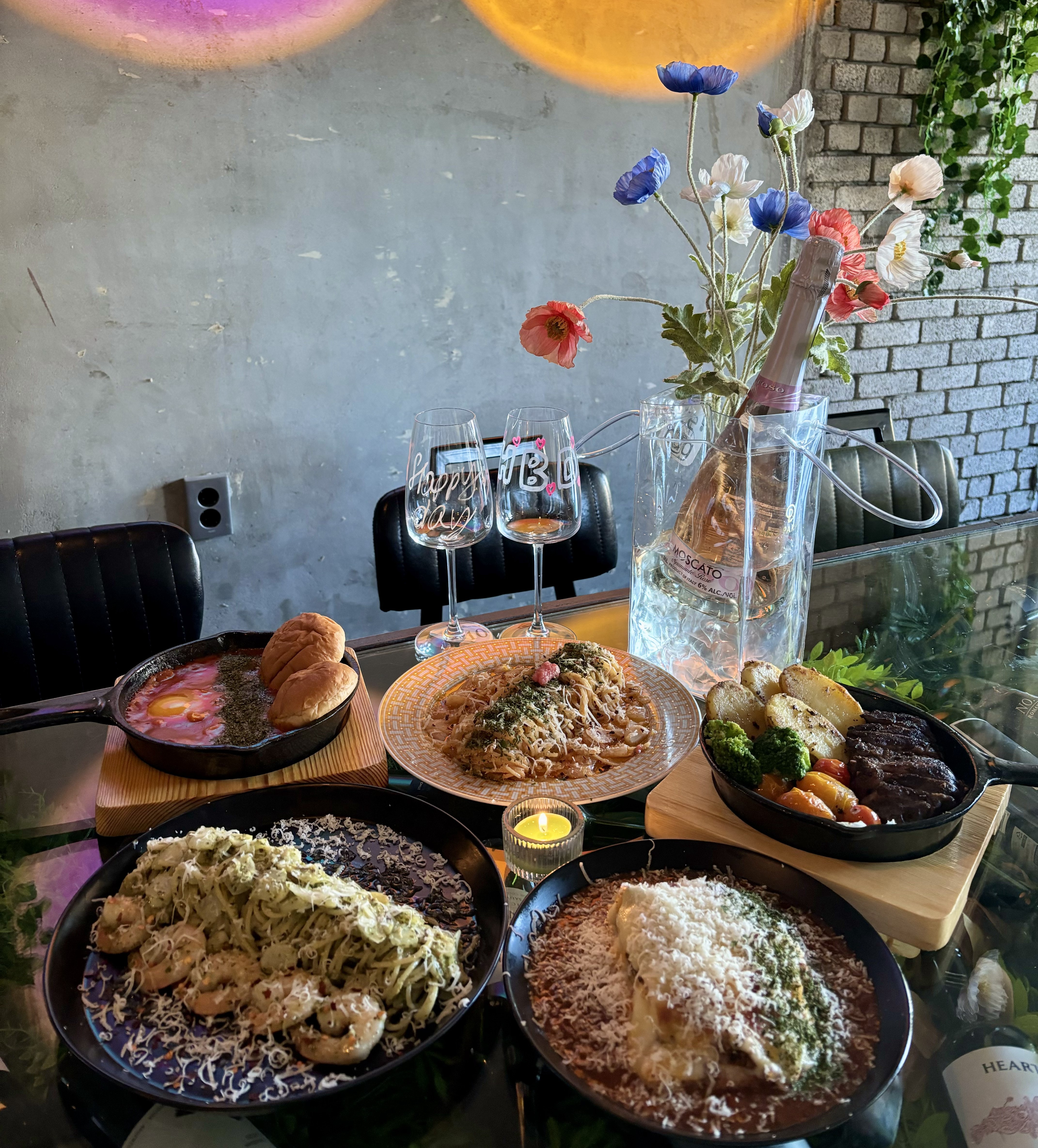Dining table spread with pasta, steak in cast iron skillet, and sparkling wine