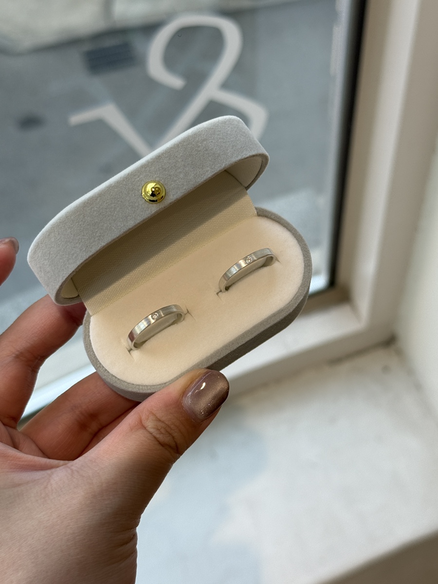 A hand holding a velvet ring box containing two silver rings with small diamonds by the studio window.