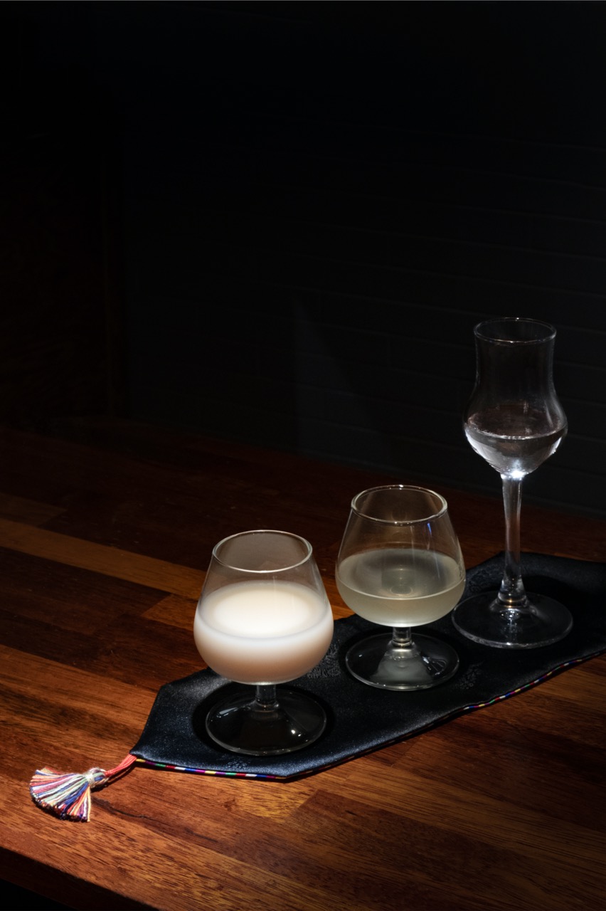 Three varying alcoholic beverages served in elegant glass cups on a dark decorative mat on a wooden table.