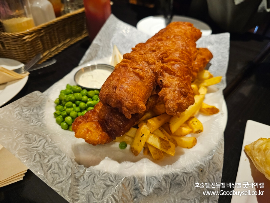 Plate of fish and chips with peas and dipping sauce served on textured paper