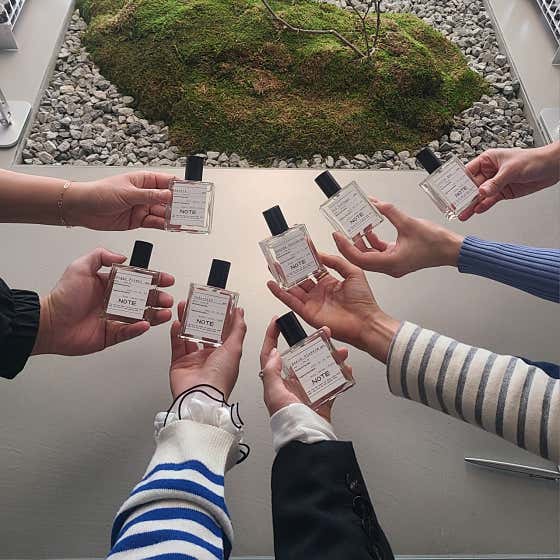 Visitors holding finished custom perfume bottles over pebble and moss installation
