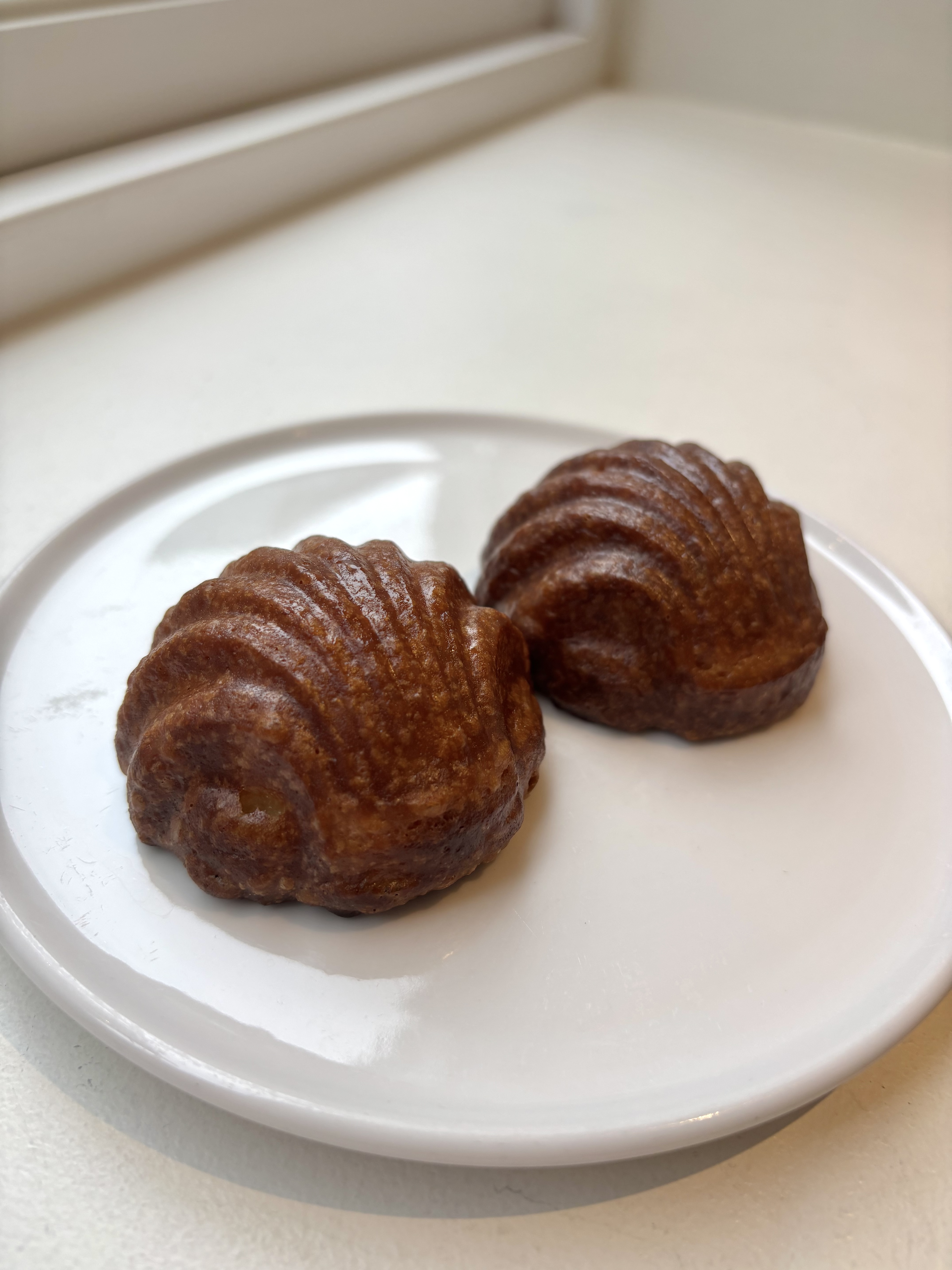 Two glossy golden shell-shaped butter tteok baked confections on white plate