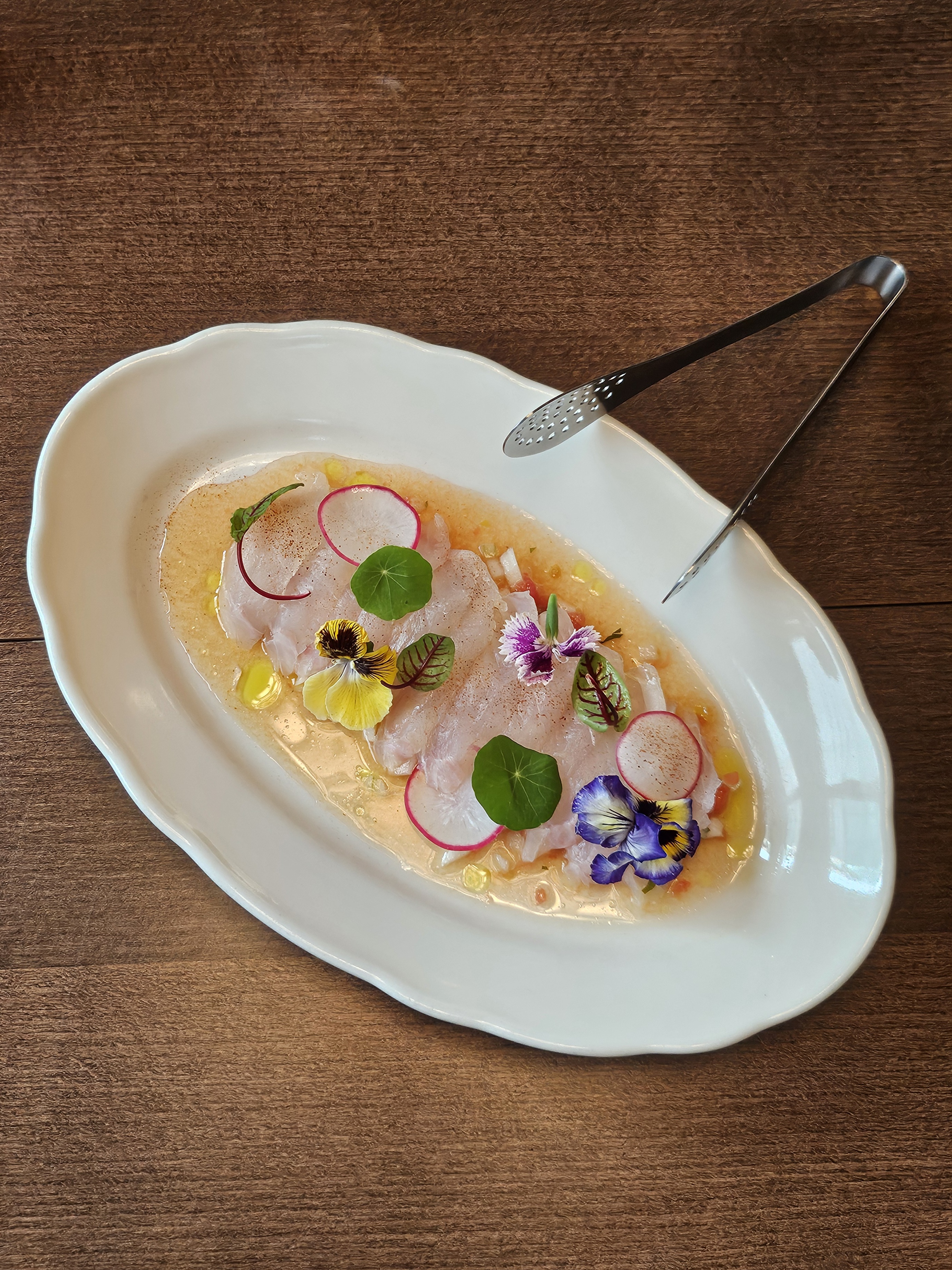 Delicate seasonal carpaccio on a white platter garnished with edible flowers and radishes