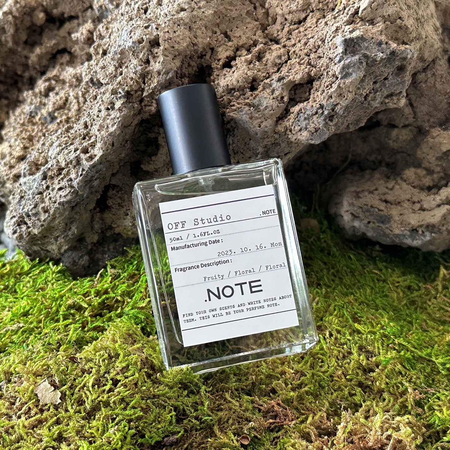 Clear .NOTE perfume bottle resting on lush moss against textured stone