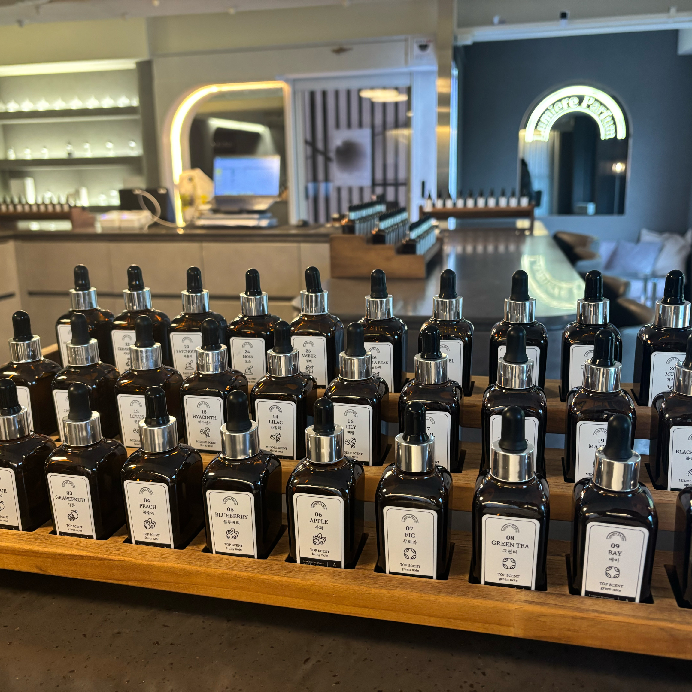 Amber perfume bottles with dropper caps arranged on a stepped wooden stand in the perfumery workshop
