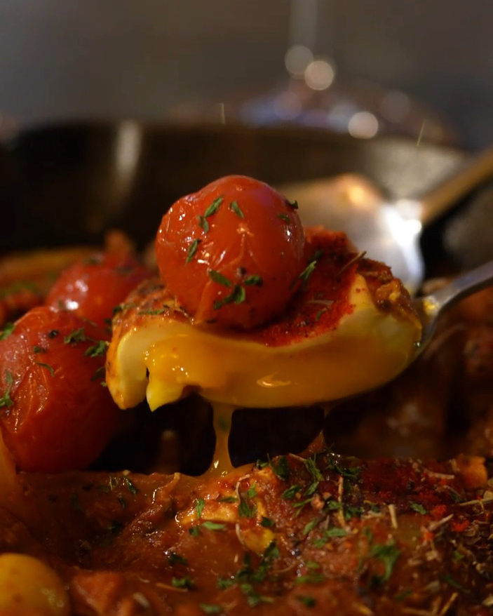 Spoon lifting soft egg yolk and cherry tomato from seasoned skillet stew