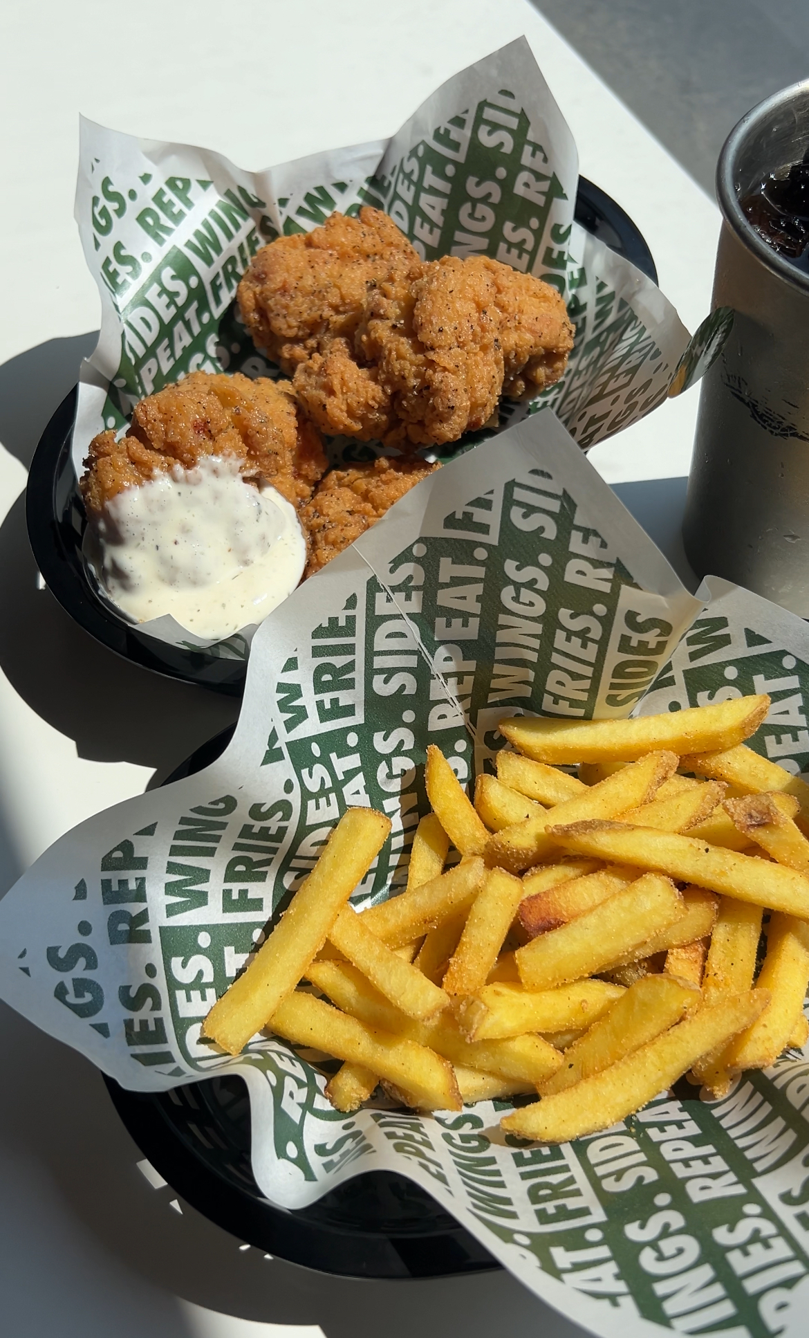 Baskets of sauced chicken and golden french fries served on branded parchment