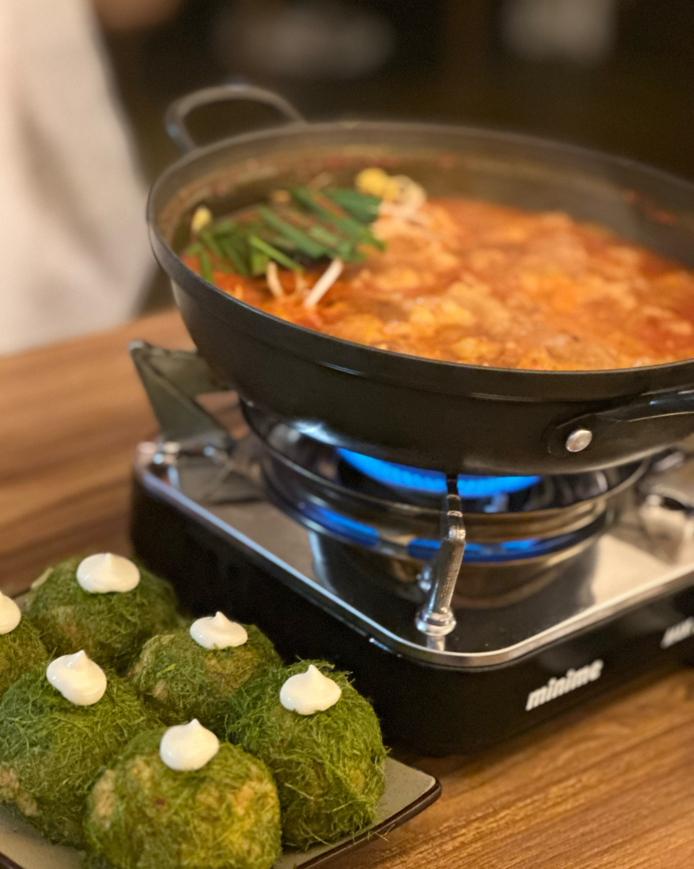 Spicy stew bubbling over a portable burner accompanied by seasoned rice balls