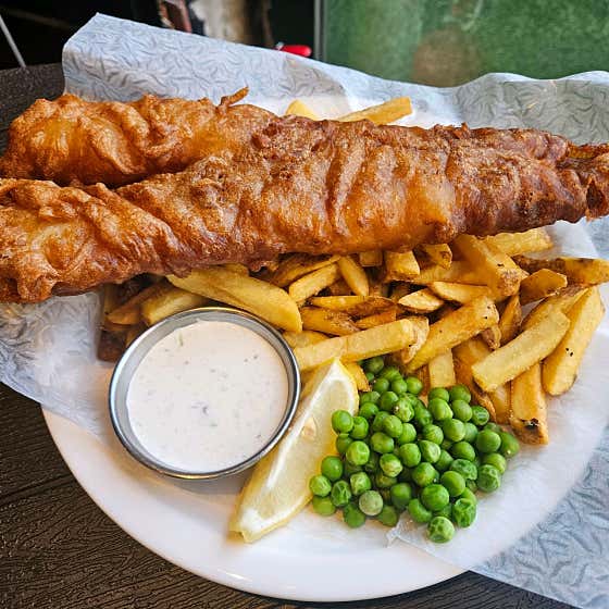 Golden battered fish and chips served with peas, tartar sauce, and lemon wedge