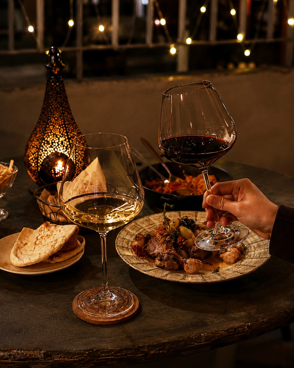 Wine glass held over dining table with Moroccan lantern glow in evening