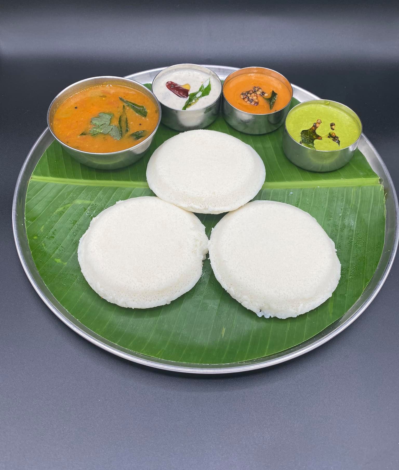 Steamed fluffy white idli rice cakes served on a fresh banana leaf with dipping sauces