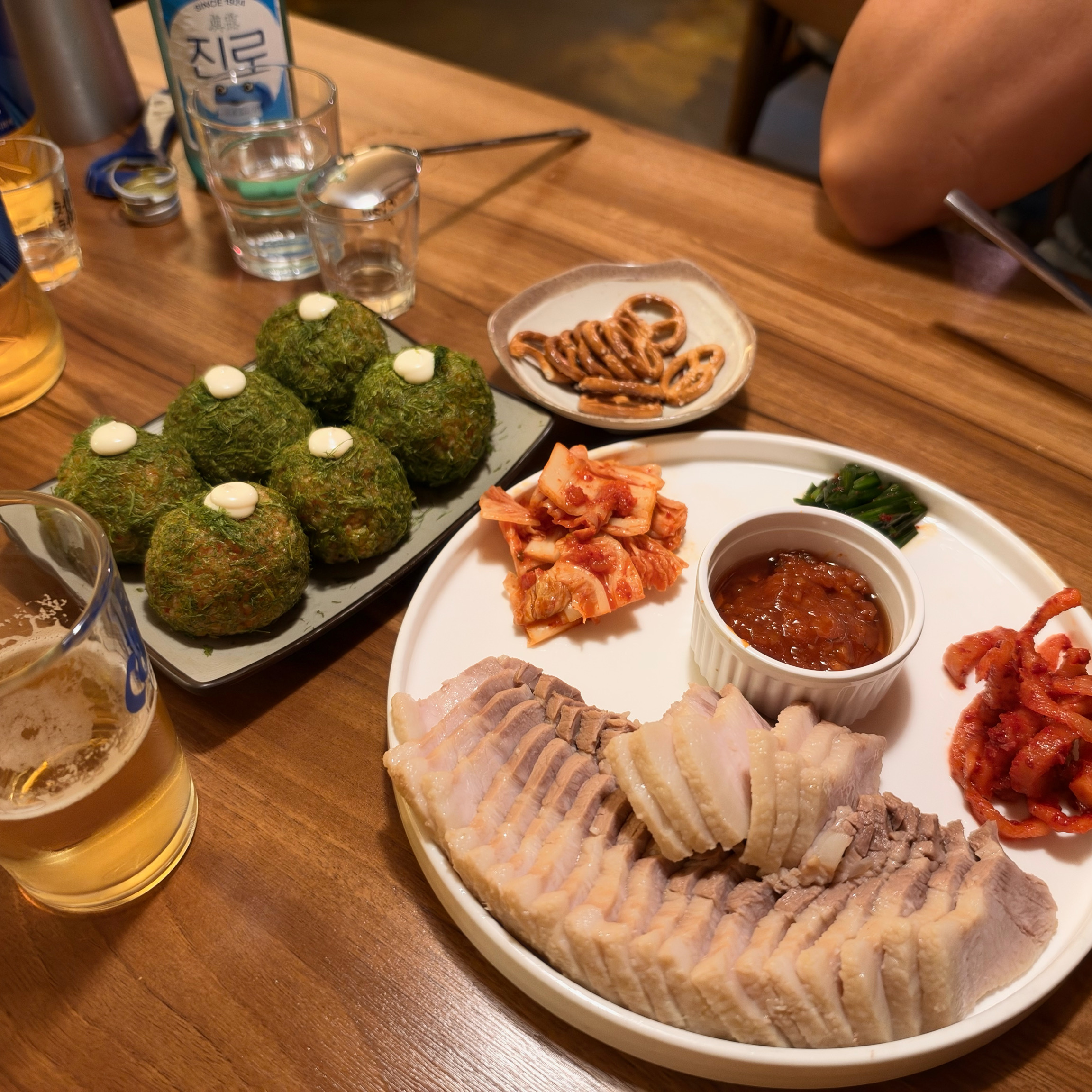 Full table spread featuring sliced pork belly, seaweed rice balls, pretzels, and beverages
