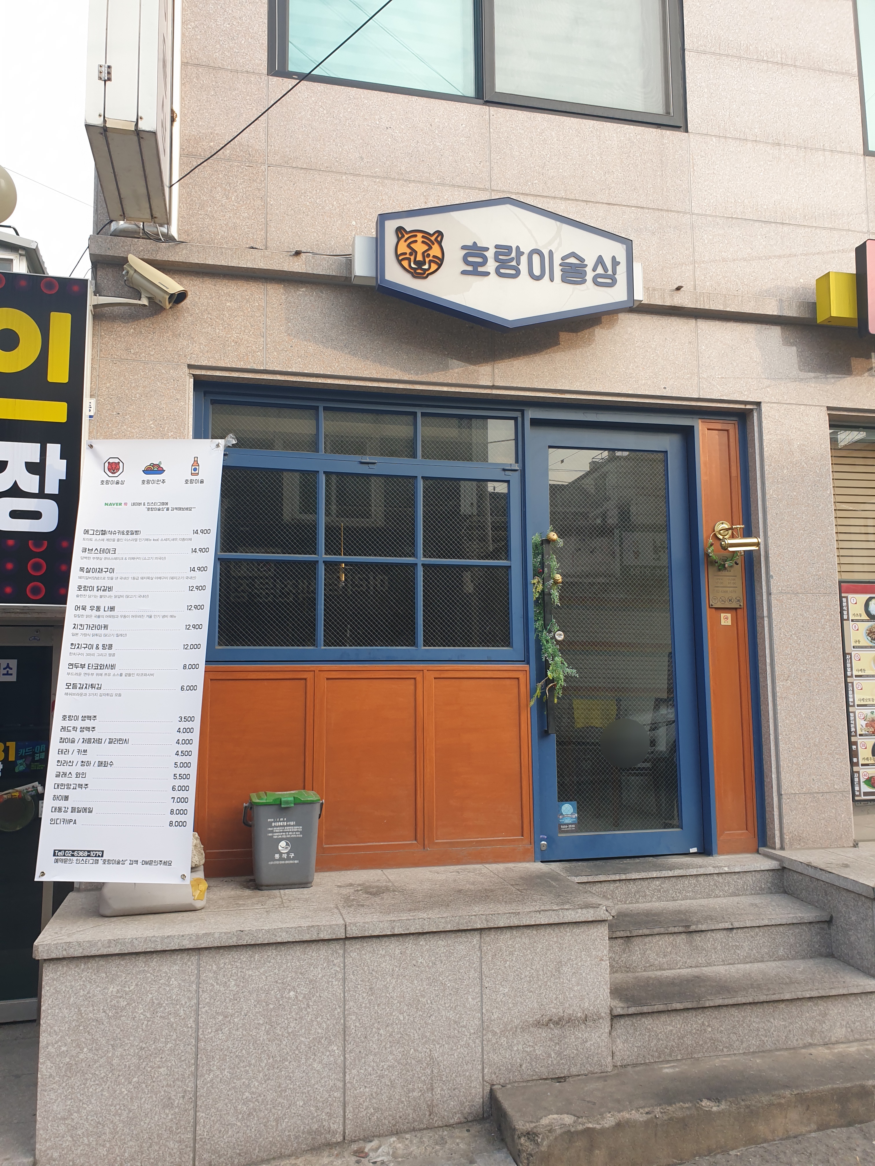 맑은 낮에 찍은 호랑이술상의 전면 입구 모습으로 푸른 도어 프레임과 화이트톤 간판이 대비를 이룬다.