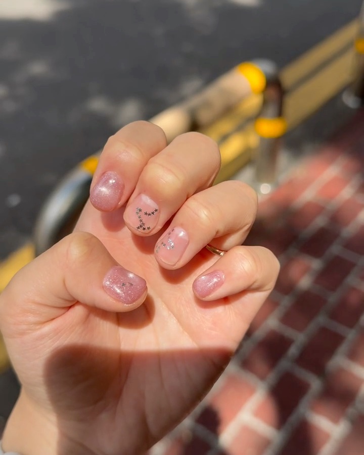 Close-up of hand showing short, glittery pink nails with small star-shaped silver embellishments