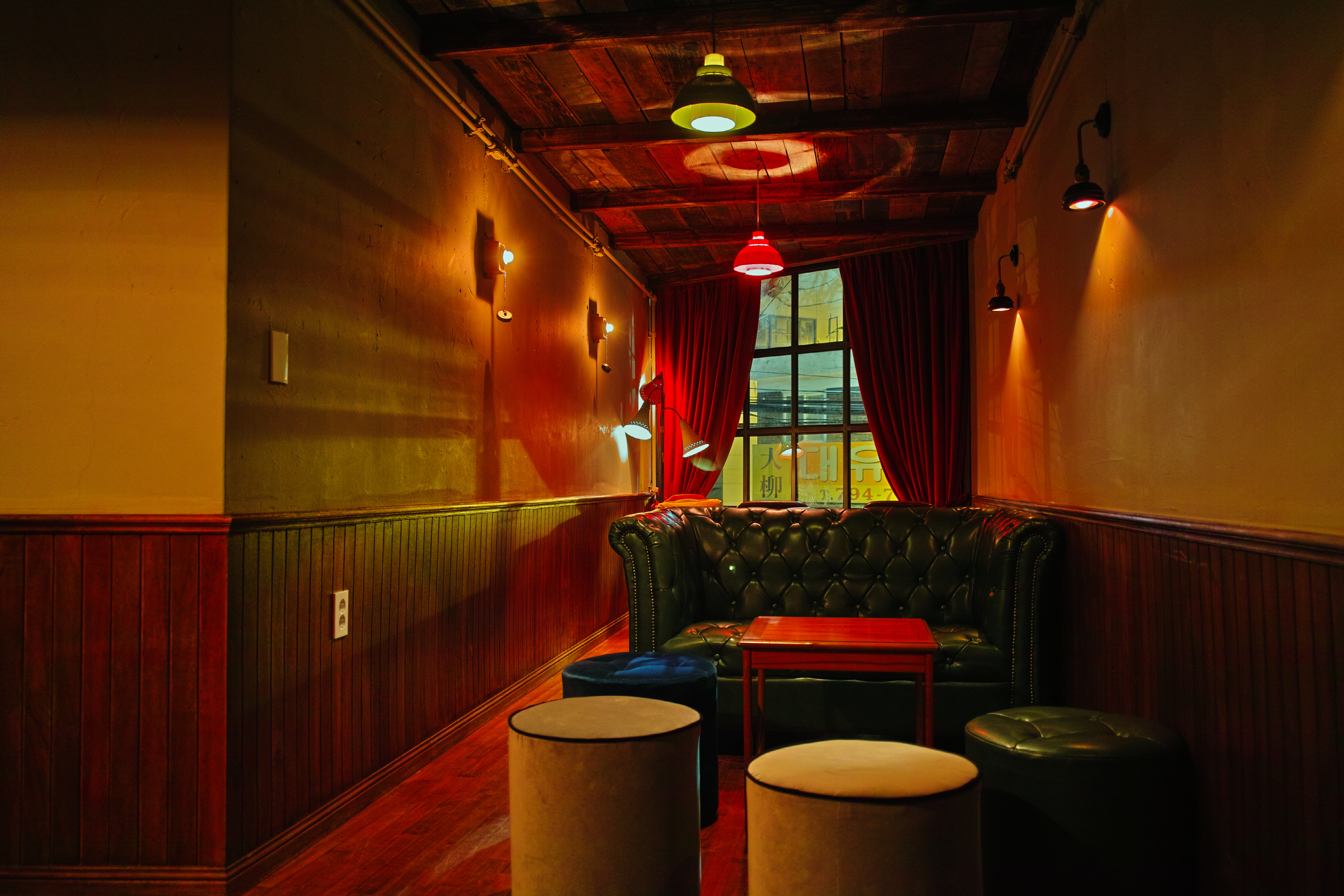 Tufted leather sofa and round upholstered stools under warm wall sconces at Apt Seoul.