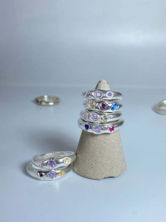 A stack of silver rings decorated with colorful star-shaped gemstones on a conical display stand