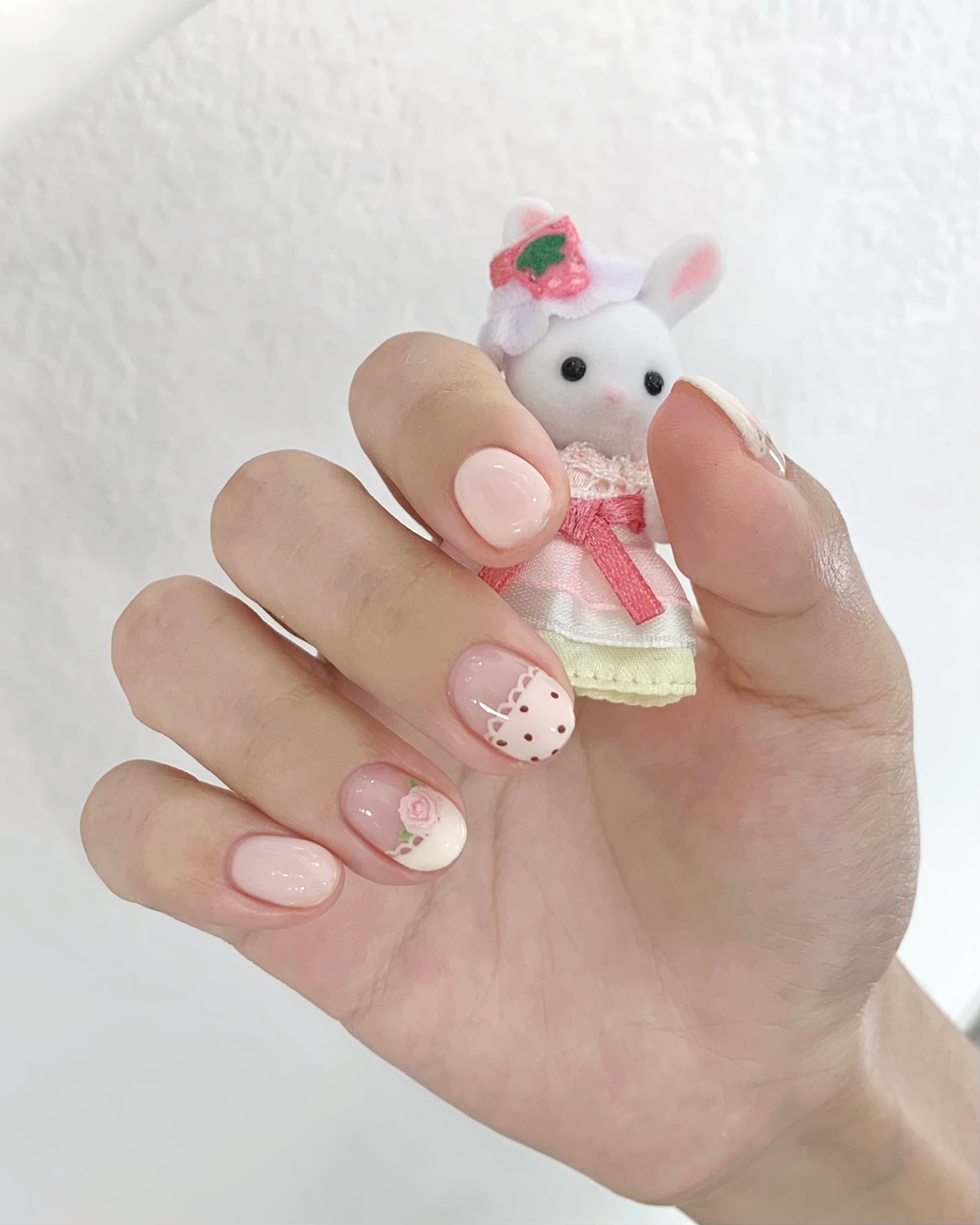 Hand-painted nail art with floral and pattern details holding a small rabbit figurine