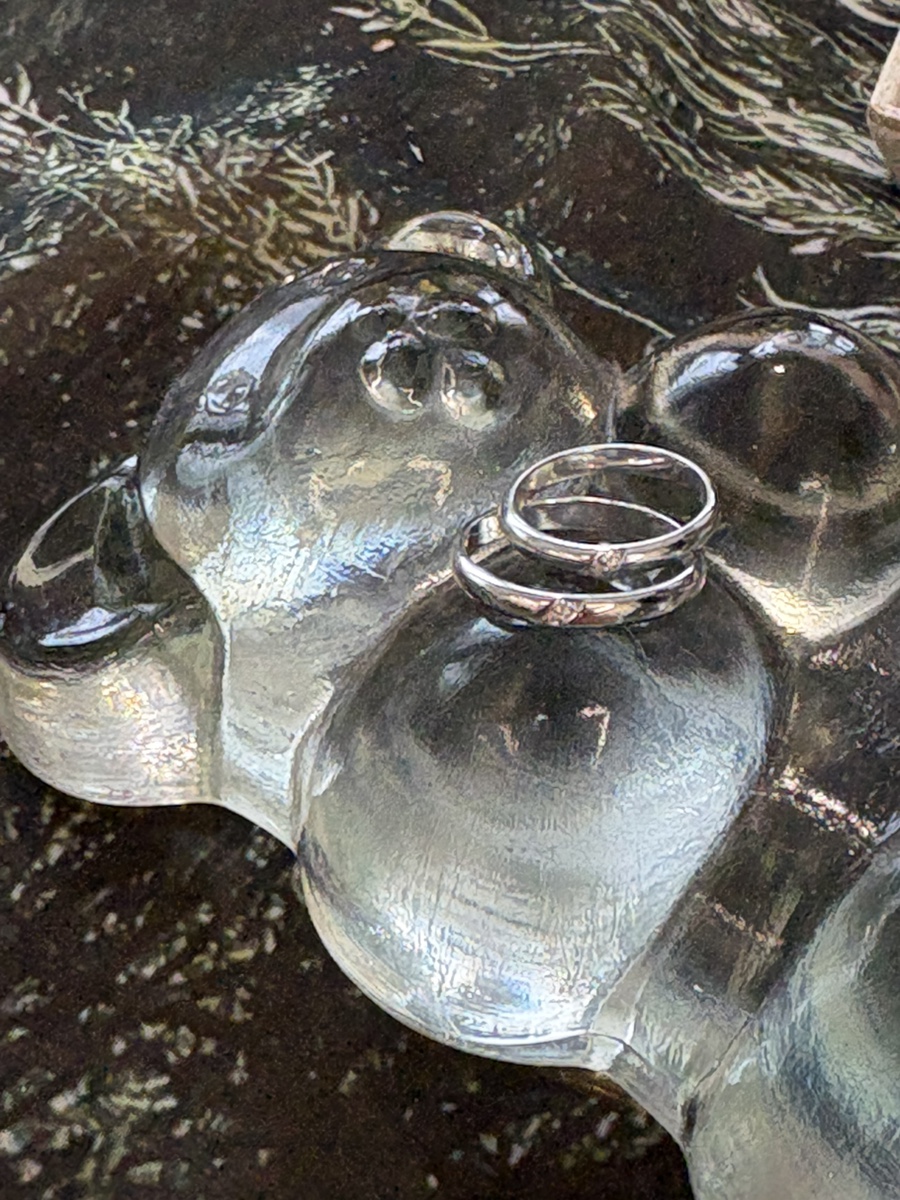 Two silver rings resting on a clear, sculpted glass bear figure
