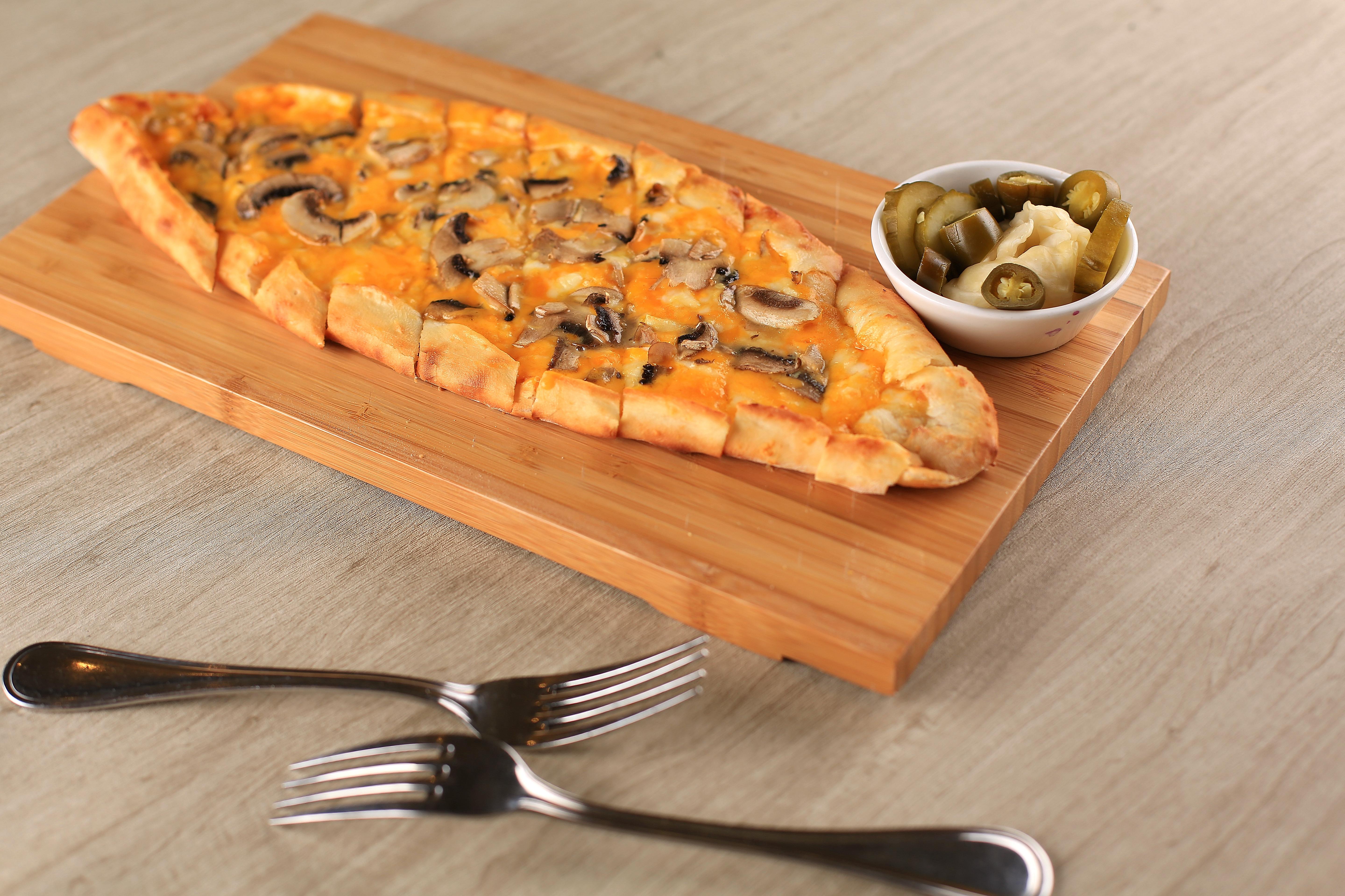 Mushroom and cheese pide on a wooden serving board with a side of pickles and jalapeños.