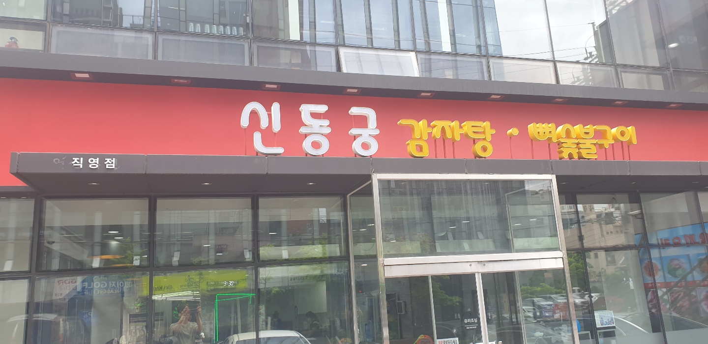 Exterior facade of Sindonggung Gamjatang restaurant with red walls and yellow Korean signage.
