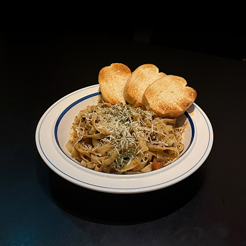 A plate of fettuccine pasta with three slices of toasted bread on a dark table.