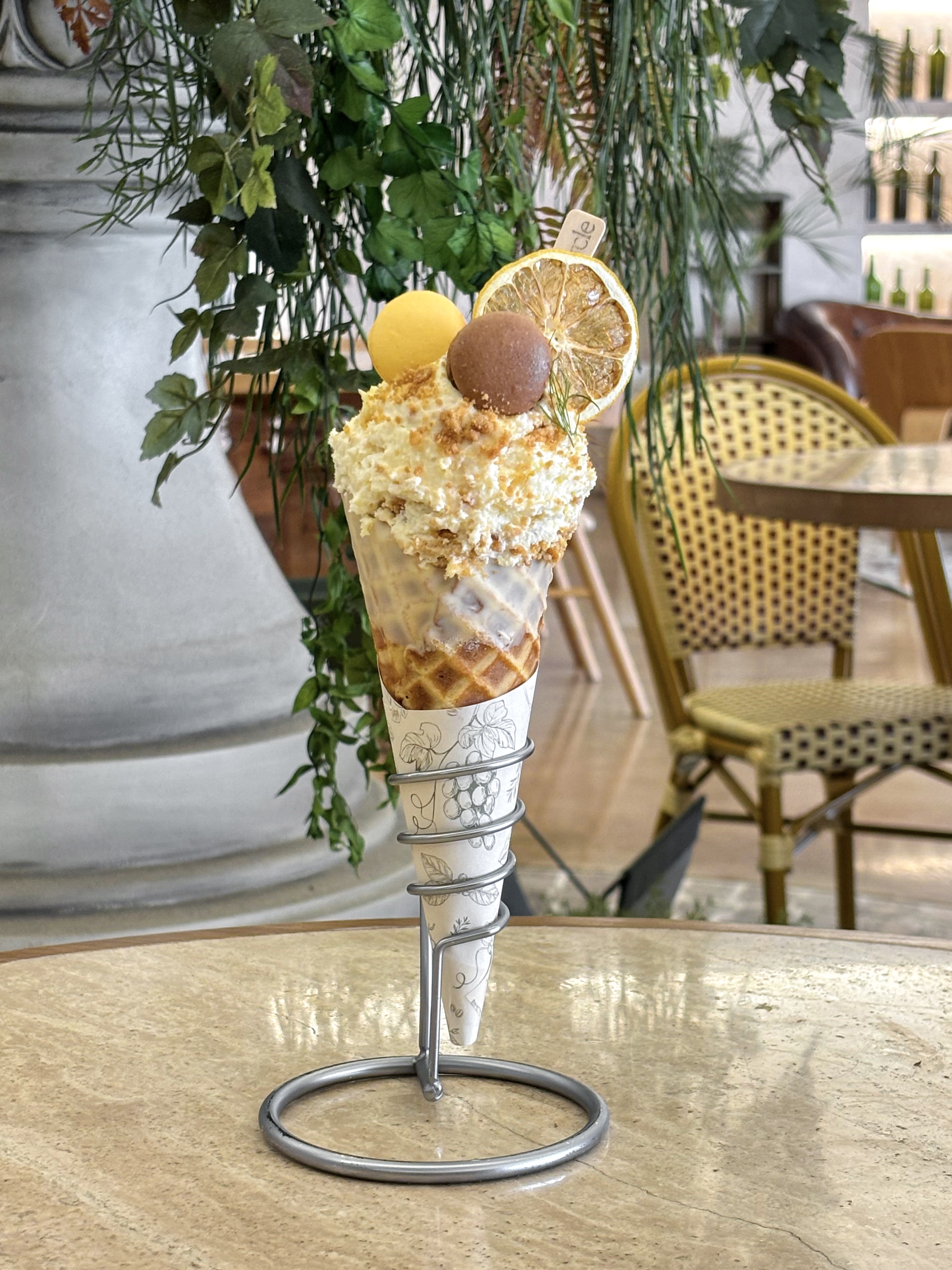A decorative brunch dessert served in a waffle cone held by a metal stand on a cafe table.