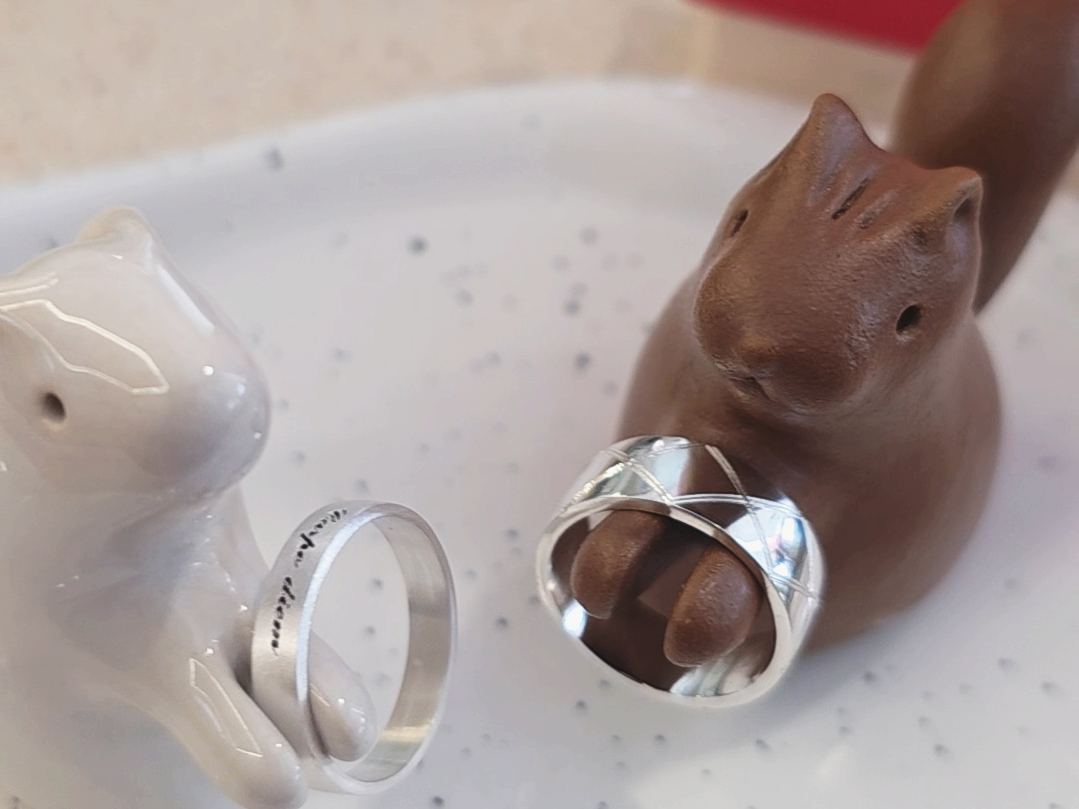 Two squirrel figurines holding silver rings on a white plate