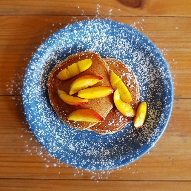 Pancakes topped with sliced peaches and powdered sugar on a blue plate