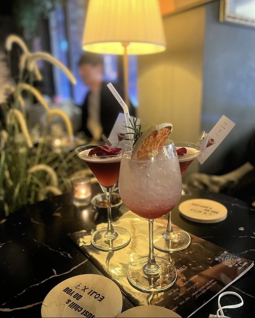 Three cocktails served on dark marble table under warm indirect lamp illumination