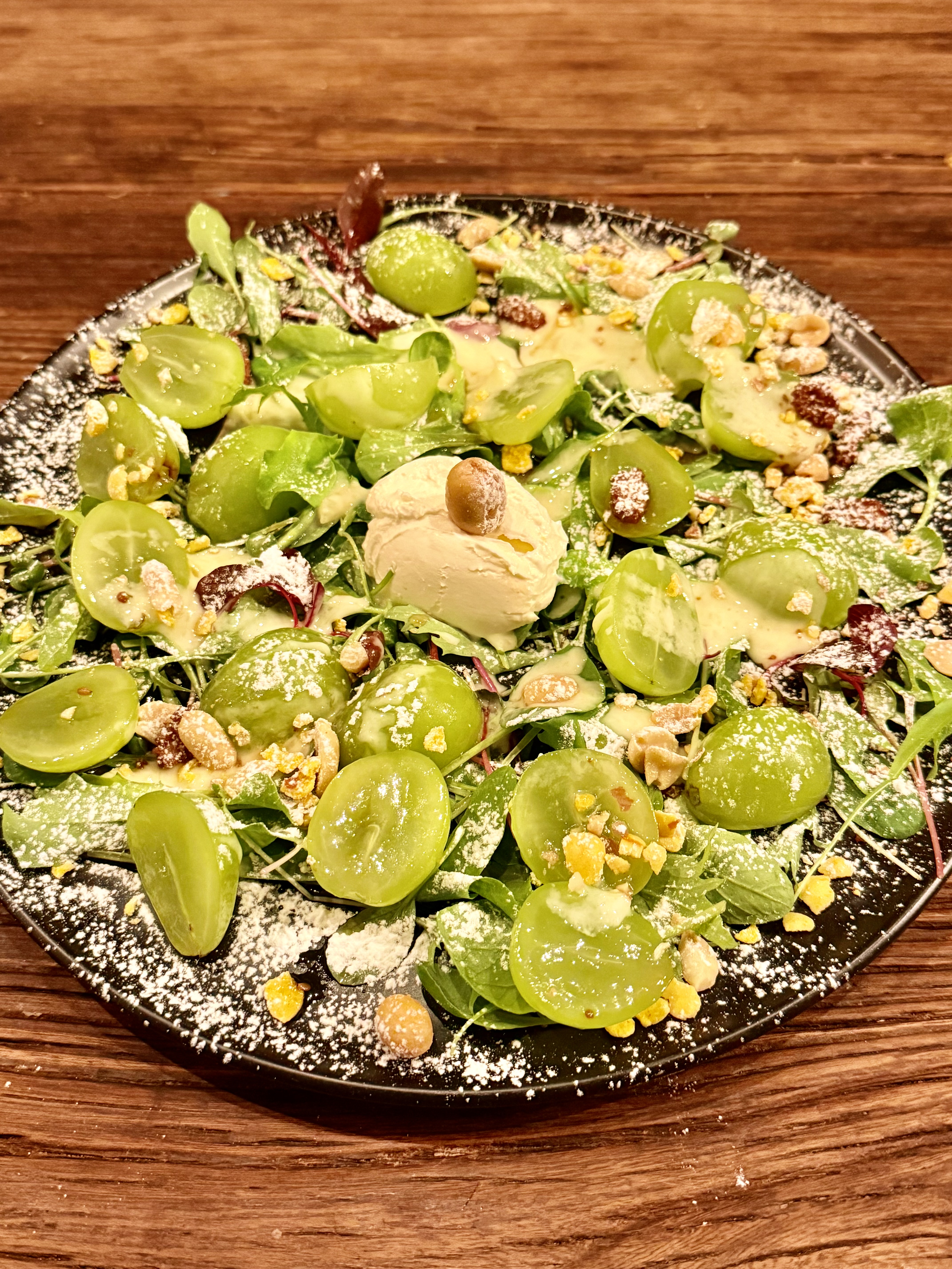 Fresh green grape salad with cream cheese scoop and crushed nuts on a black ceramic plate