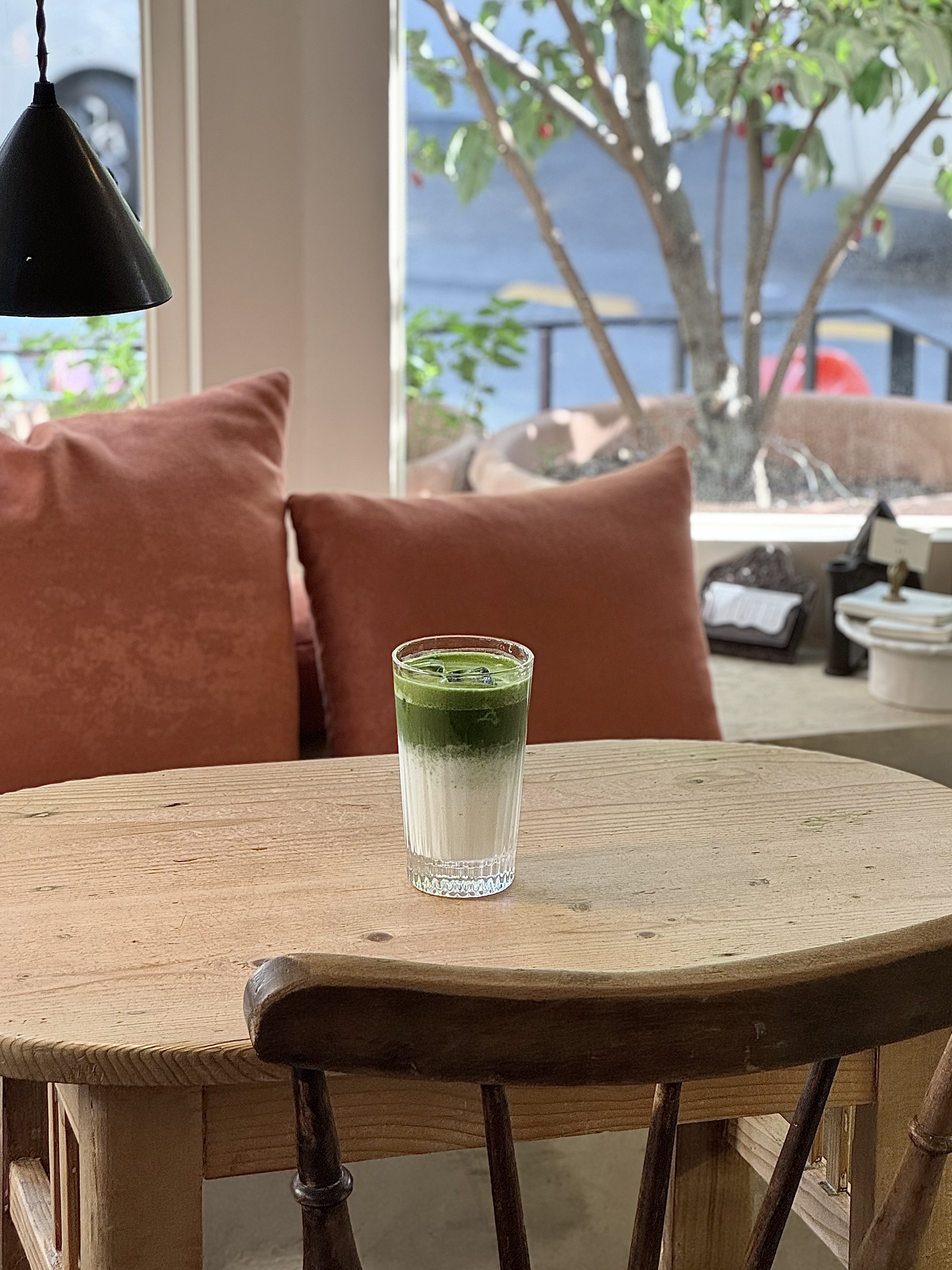 Layered iced matcha latte in a clear glass by sunlit cushions