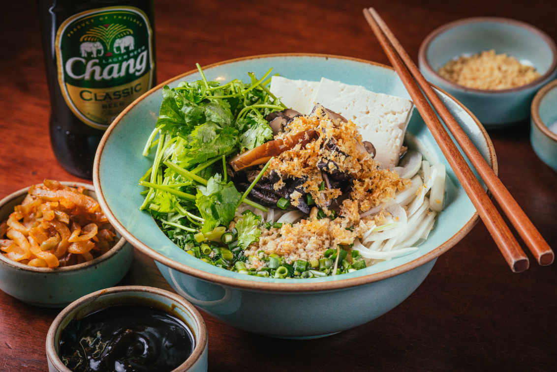 Bowl of Thai noodle soup topped with tofu and herbs