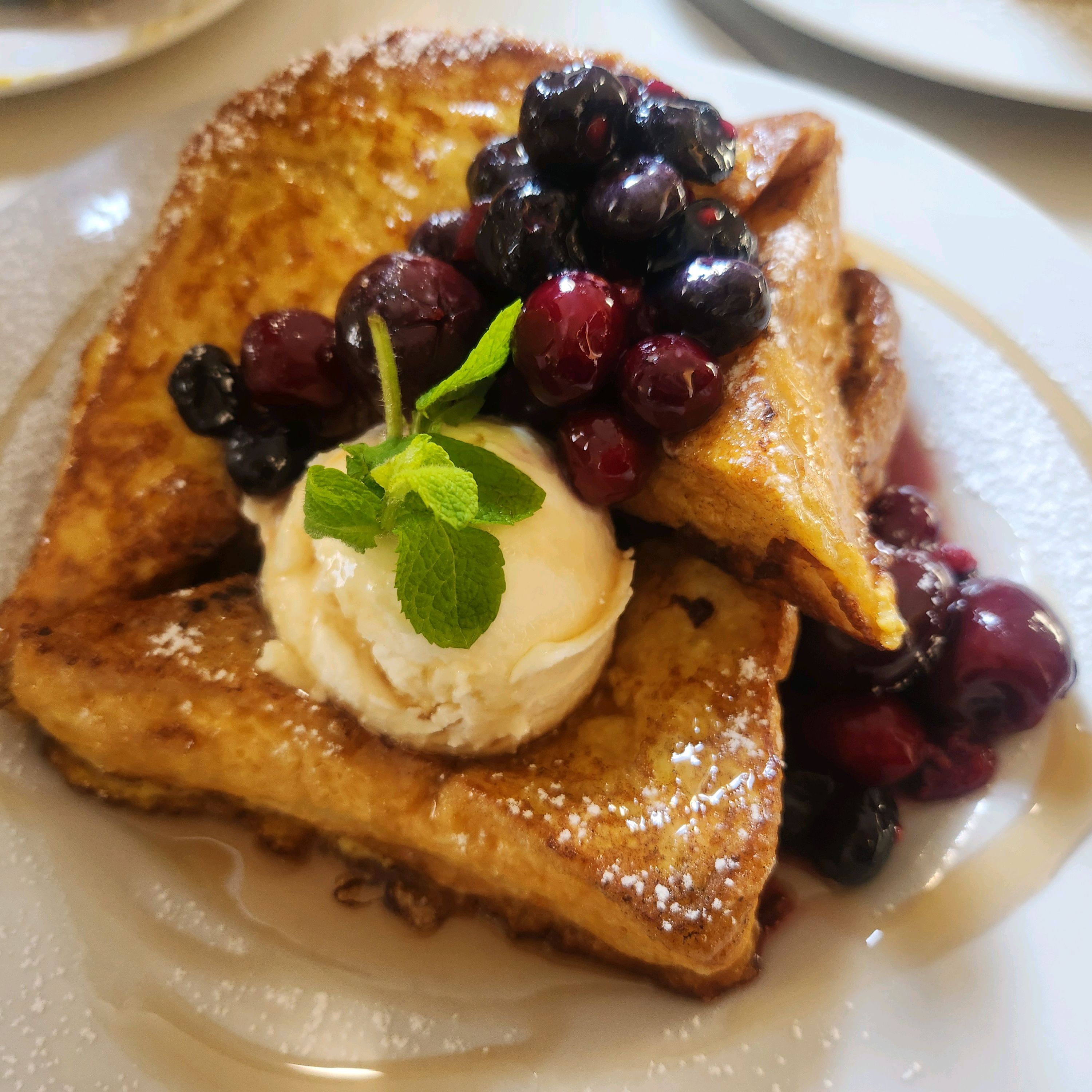 French toast topped with ice cream, mixed berries, and mint on a white plate