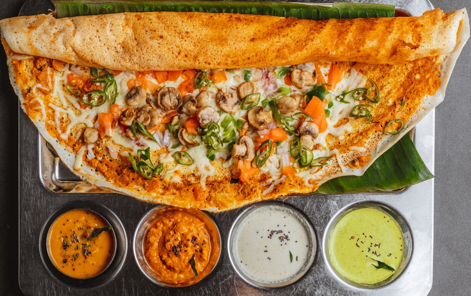 Crispy golden folded dosa served on a banana leaf tray with assorted fresh chutneys