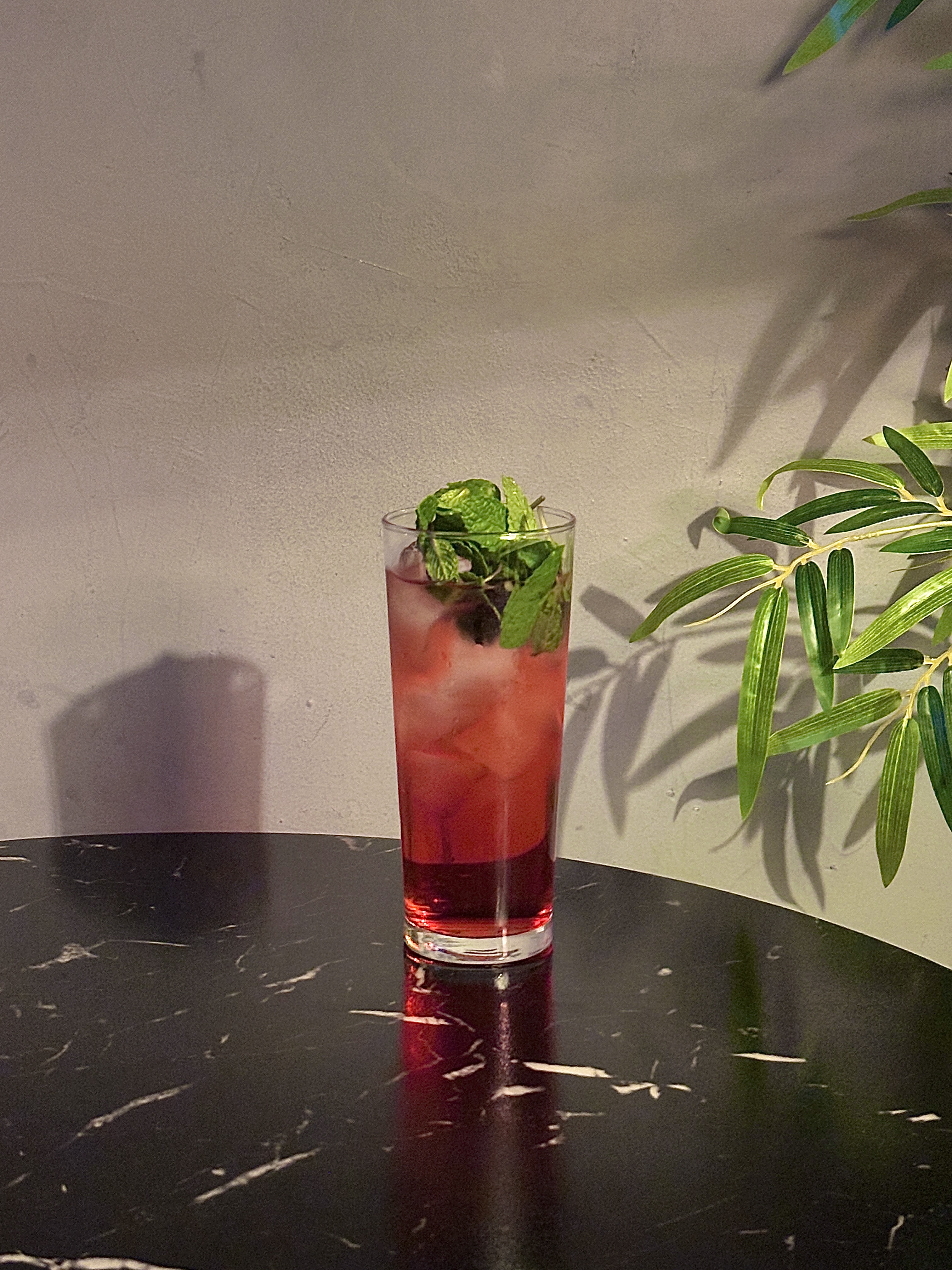 Tall red cocktail with crushed ice and fresh mint leaves on dark table