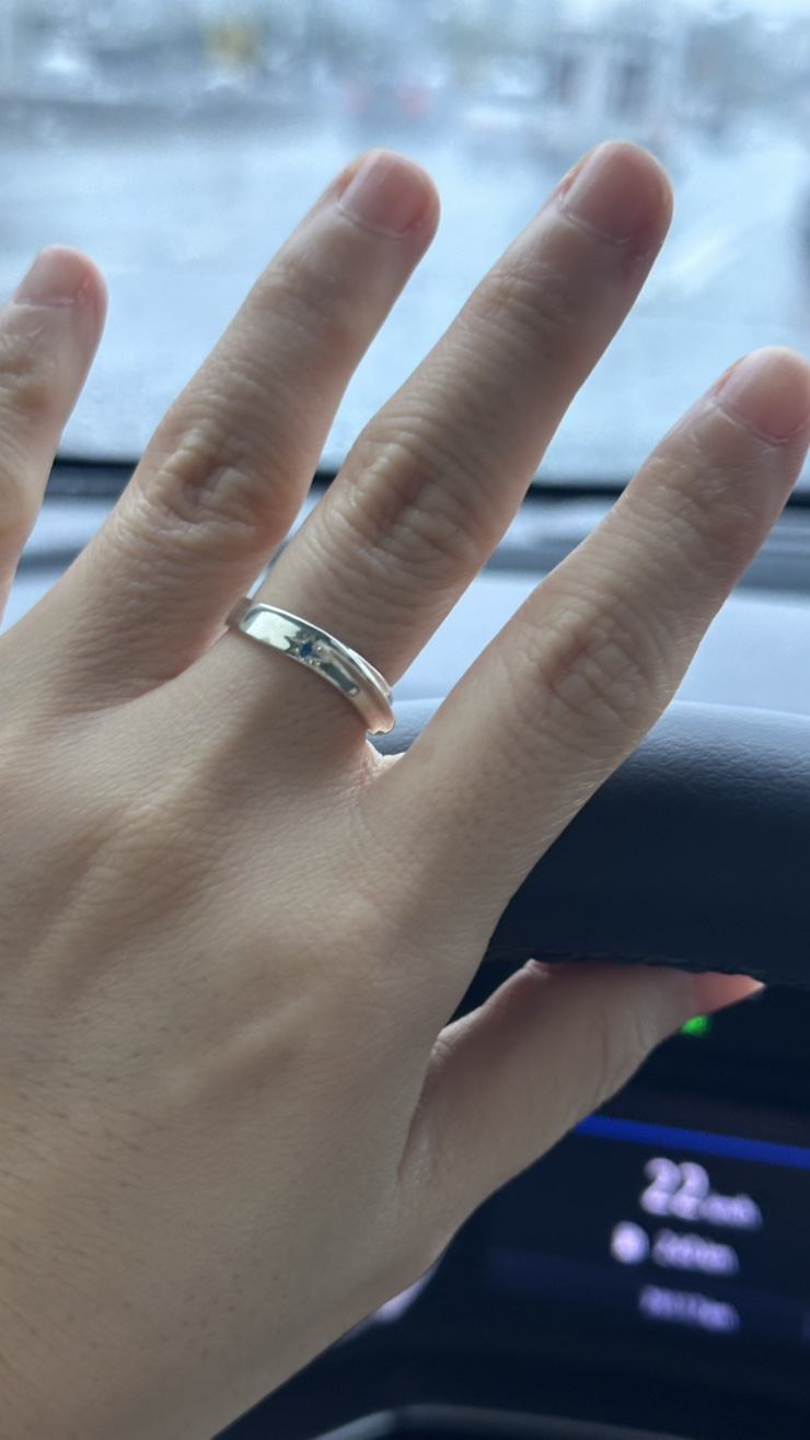 A silver ring with a small blue stone on a person's finger