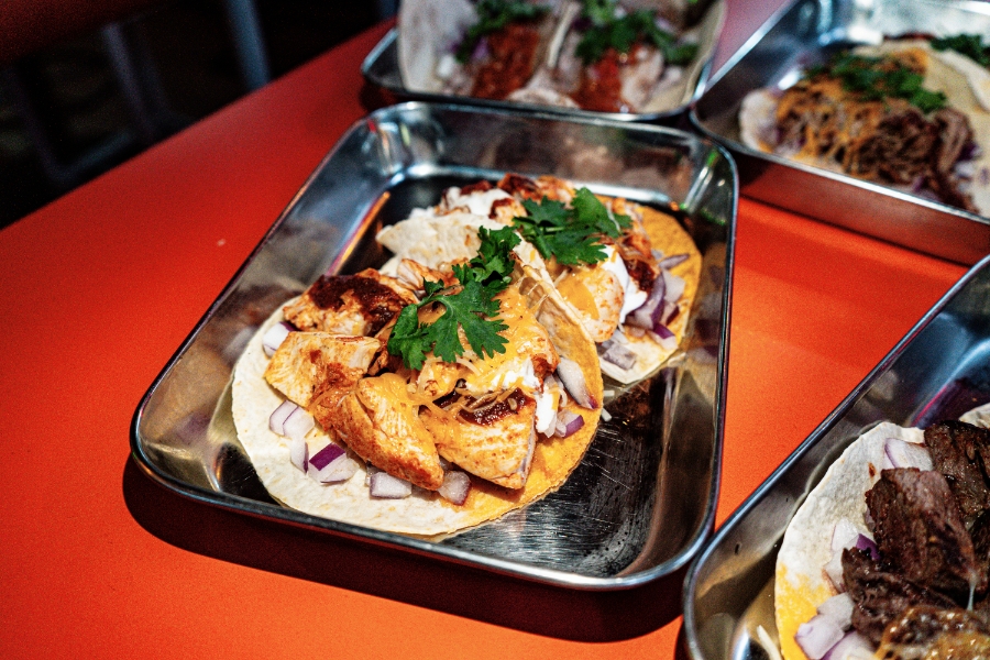 Assorted tacos with diced onions, cheese, and cilantro on metal serving trays
