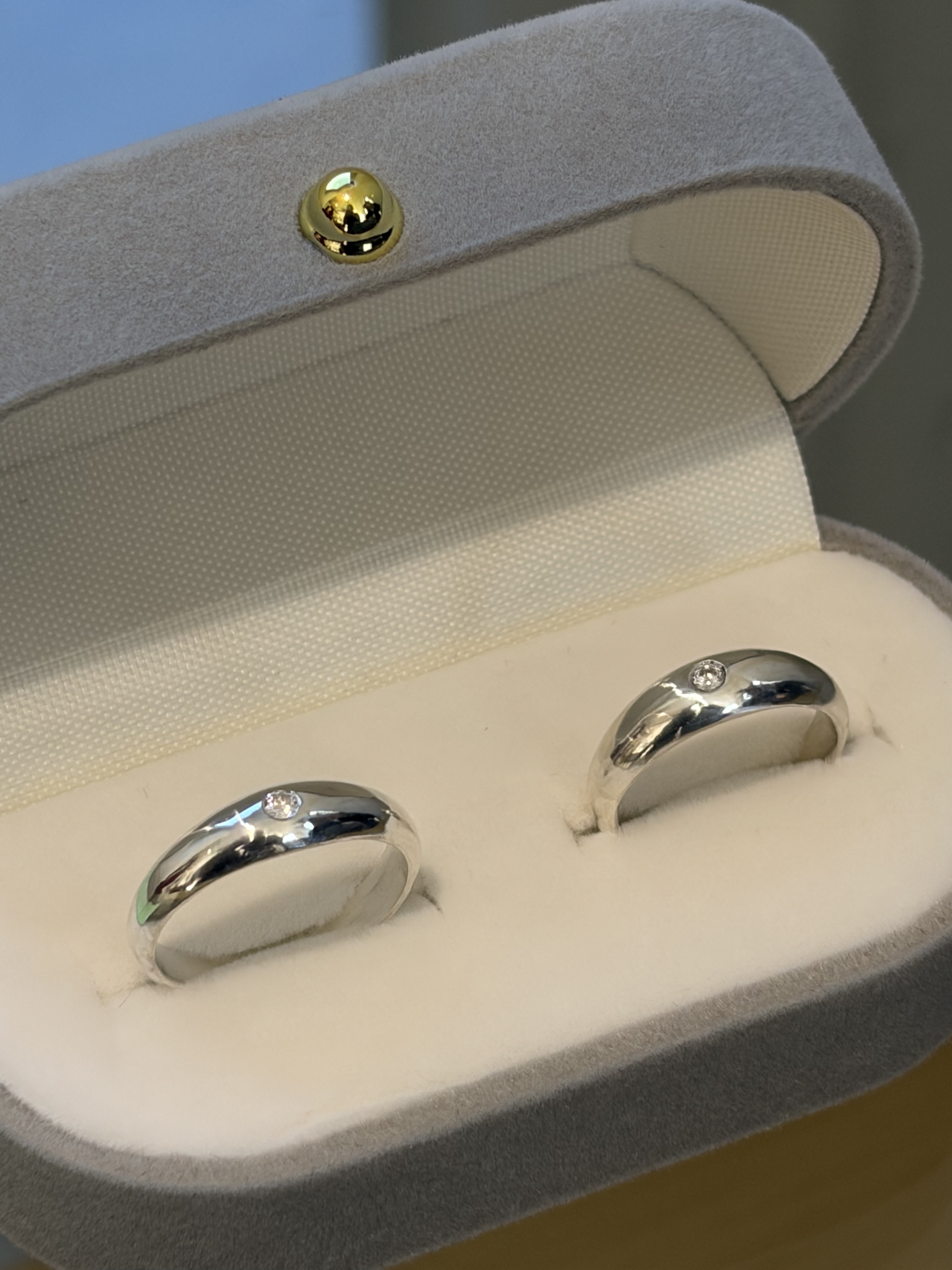 Two silver rings with embedded stones inside an open grey velvet jewelry box.