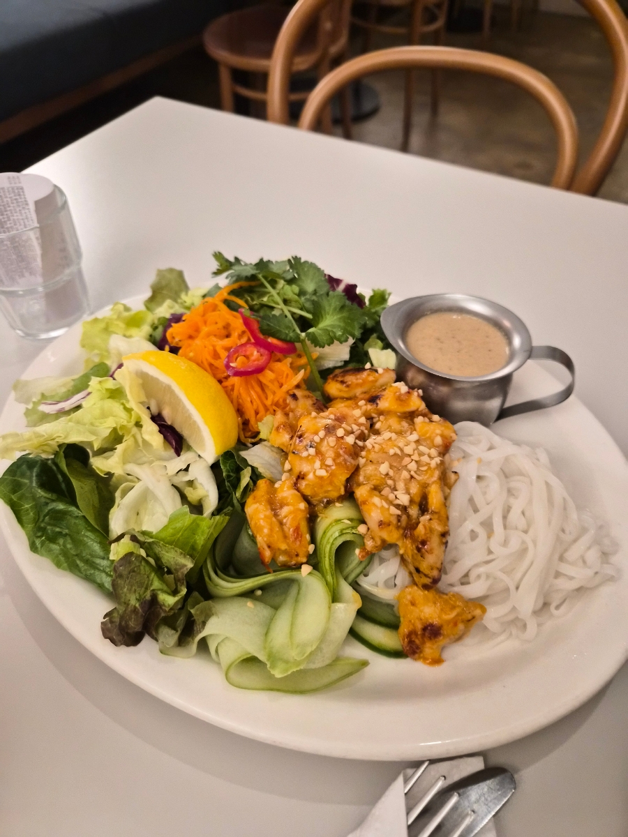 A plate of chicken noodle salad with fresh vegetables and a side of dressing at Oasis Hannam