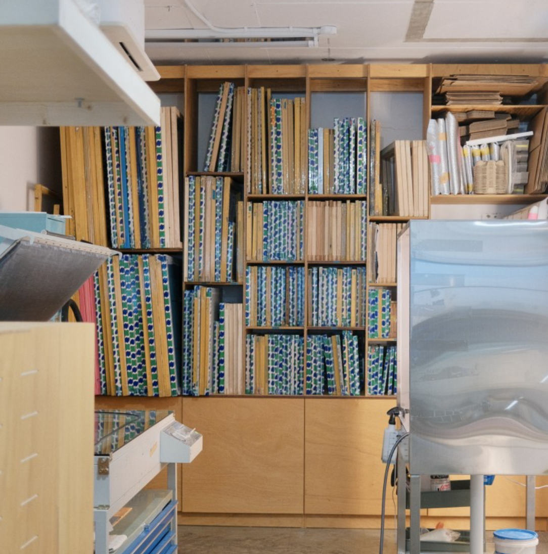 Wooden shelving unit in a workshop filled with numerous screen printing frames and supplies.