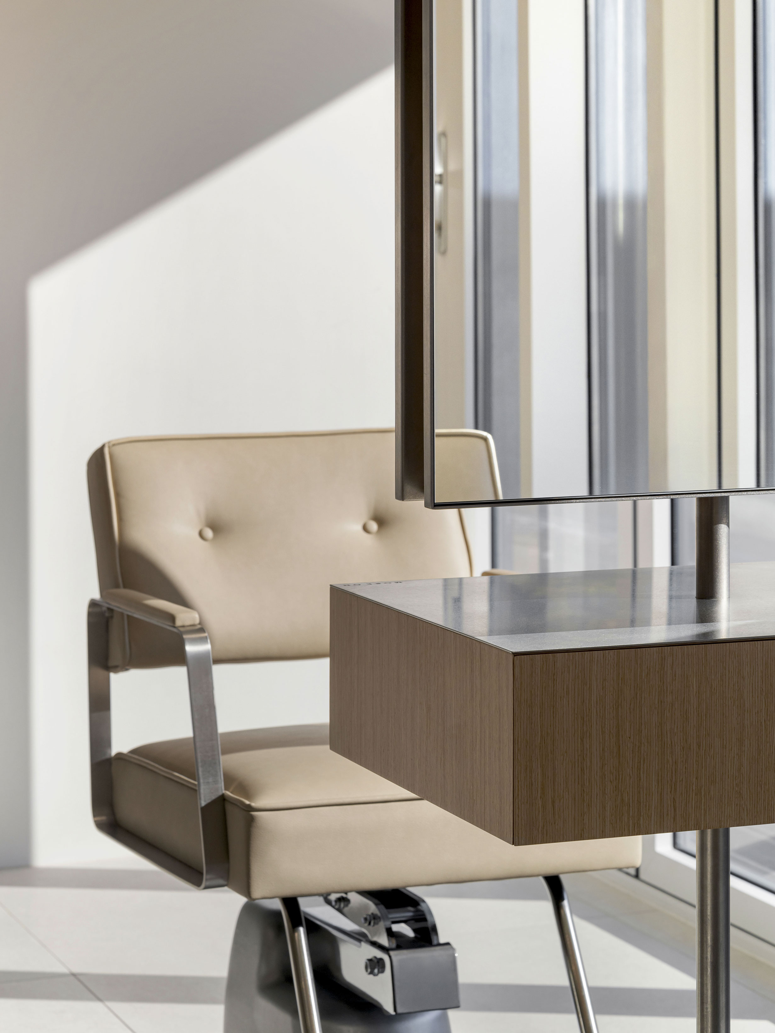 A beige salon chair with a minimalist mirror and console unit in a brightly lit studio space at MORE ON HAIR.