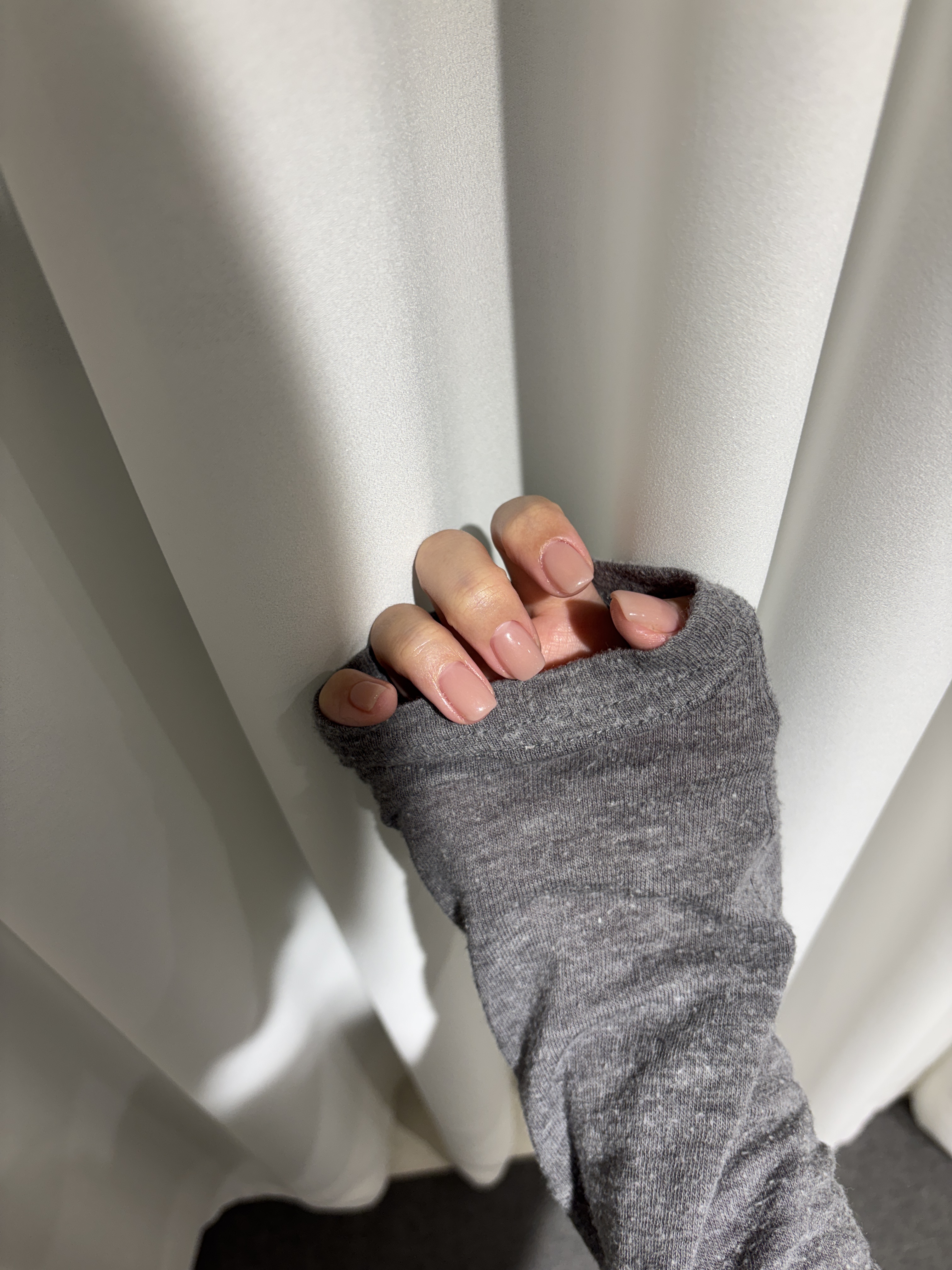 Manicured glossy neutral nude gel nails against soft white fabric