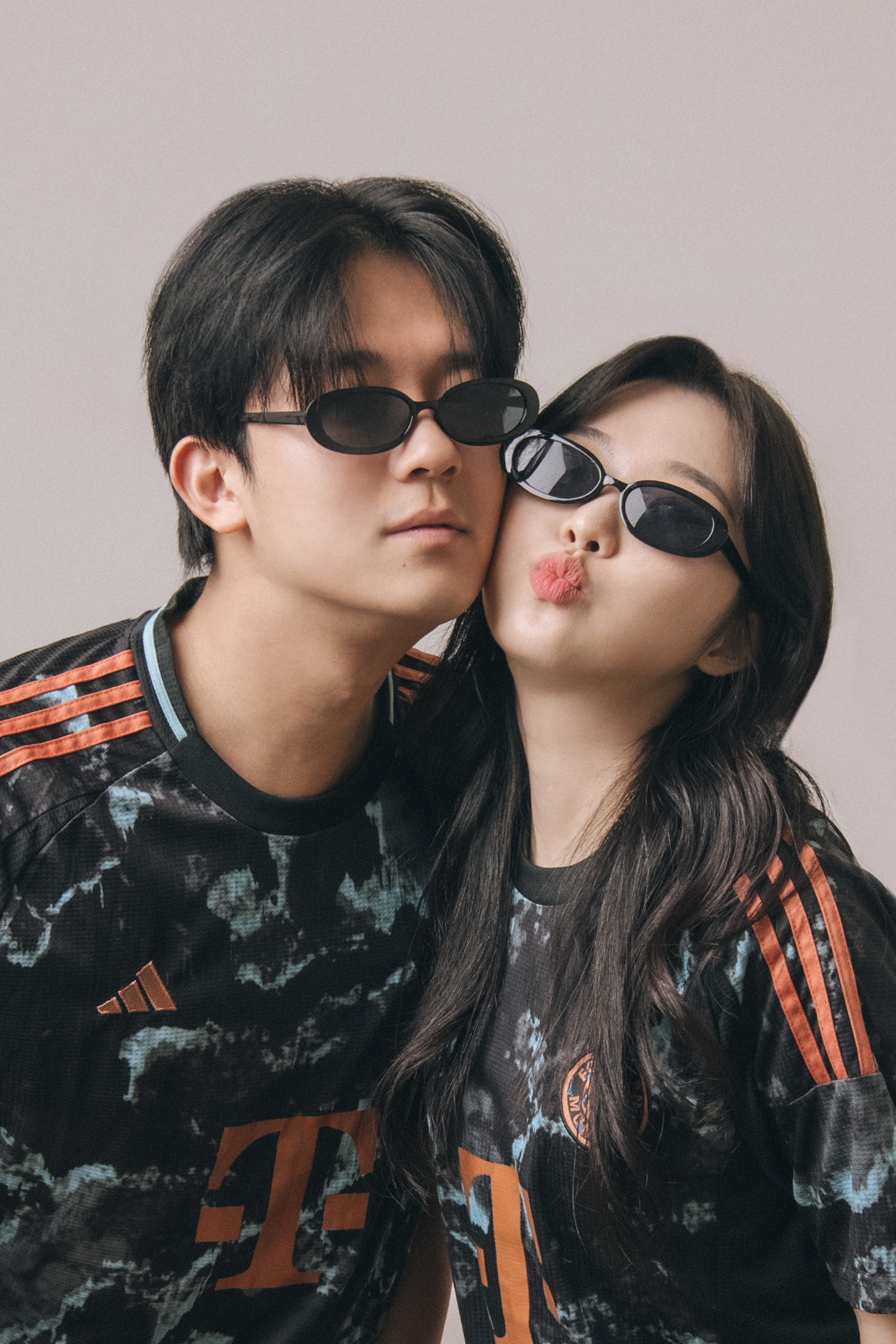 Two people wearing matching sports jerseys and black sunglasses posing for a studio portrait