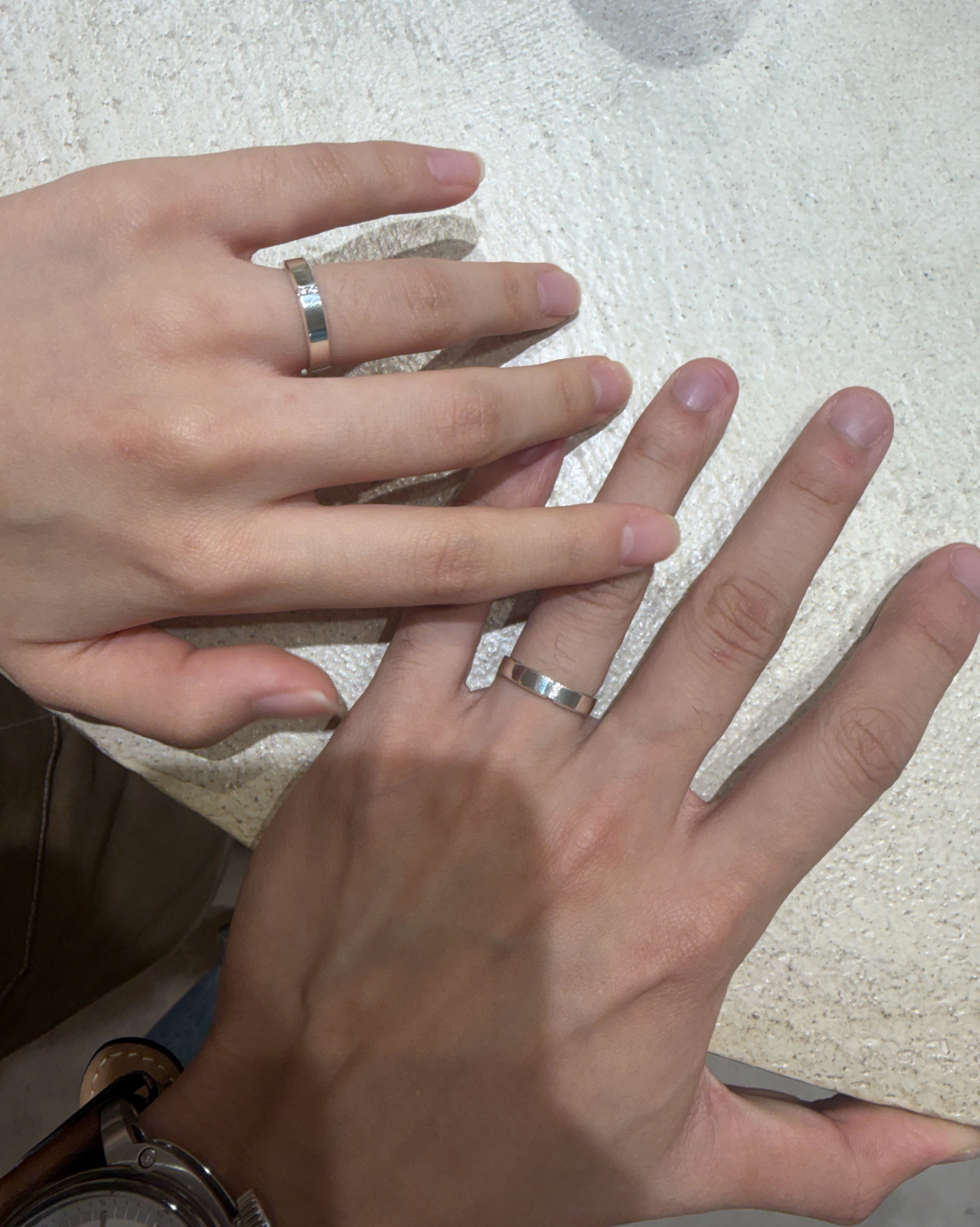 Handcrafted silver couple bands worn on hands resting together on textured light stone surface
