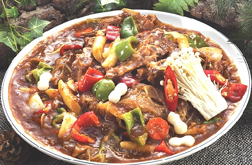 A plate of spicy stir-fried pork bones with vegetables, glass noodles, and enoki mushrooms.